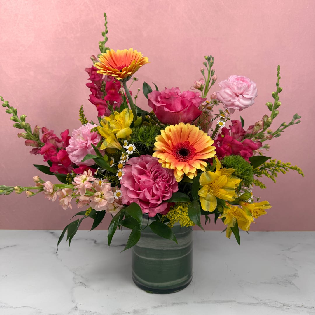 Bright &amp; Cheerful Cylinder - A bold and lively arrangement filled with bright, colorful blooms that feel joyful and uplifting. Our designers create each piece using the freshest flowers available, ensuring a dynamic and one-of-a-kind look.  Arranged in a taller cylinder vase, this design offers added height and impact, making it a customer favorite.  Available in three sizes. For a fuller, more eye-catching arrangement, we recommend upgrading to Deluxe or Premium.