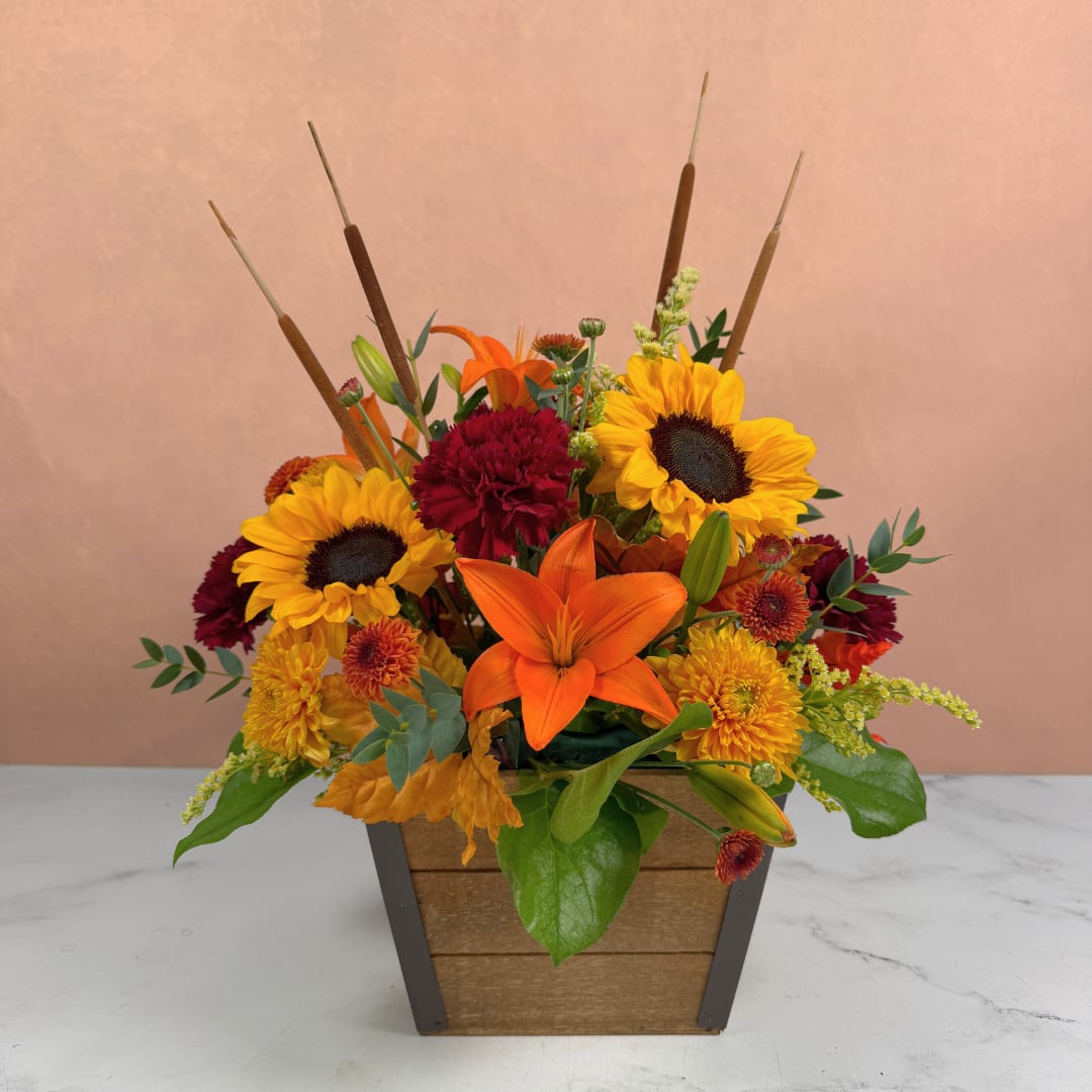 Autumn flower arrangement with sunflowers, lilies, and mums in a wooden planter