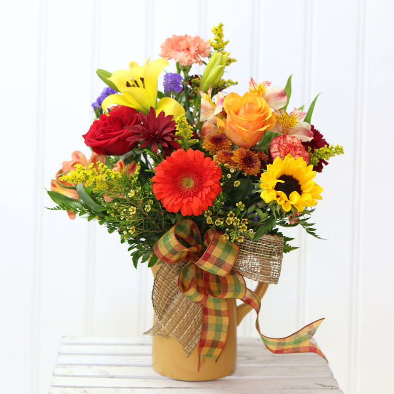 Colorful mixed bouquet in a tan pitcher with a plaid ribbon