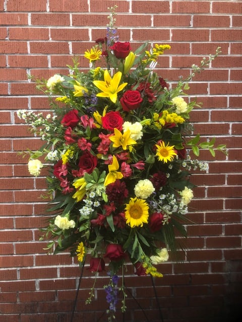 Standing floral spray with red roses, yellow lilies, and sunflowers