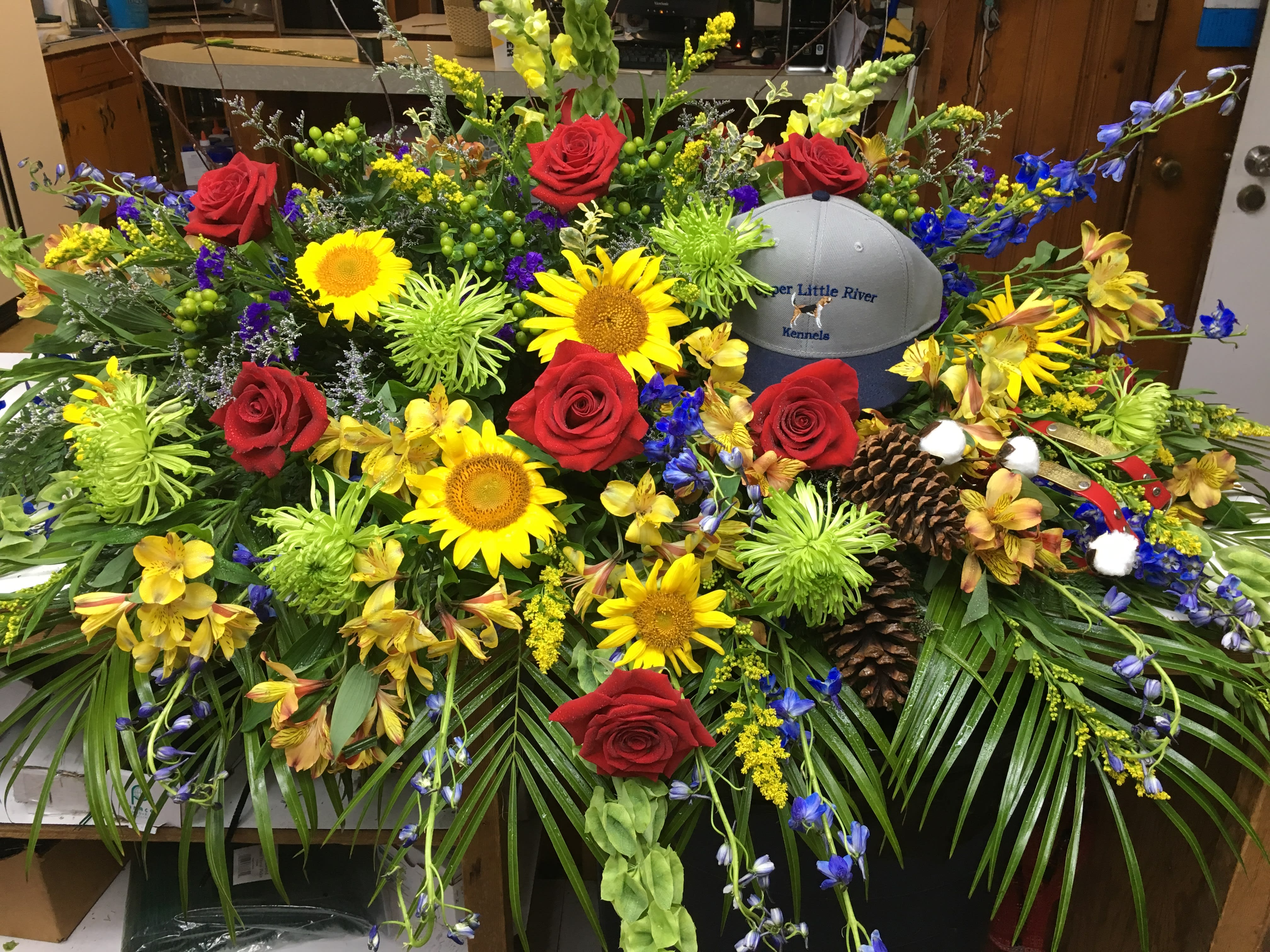 Large floral arrangement with red roses, sunflowers, and a gray baseball cap