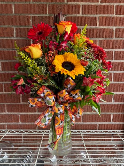 Colorful bouquet of sunflowers, roses, and gerbera daisies in a glass vase