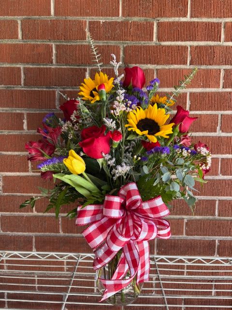 Bouquet of red roses, sunflowers, and tulips in a glass vase with a checkered bow