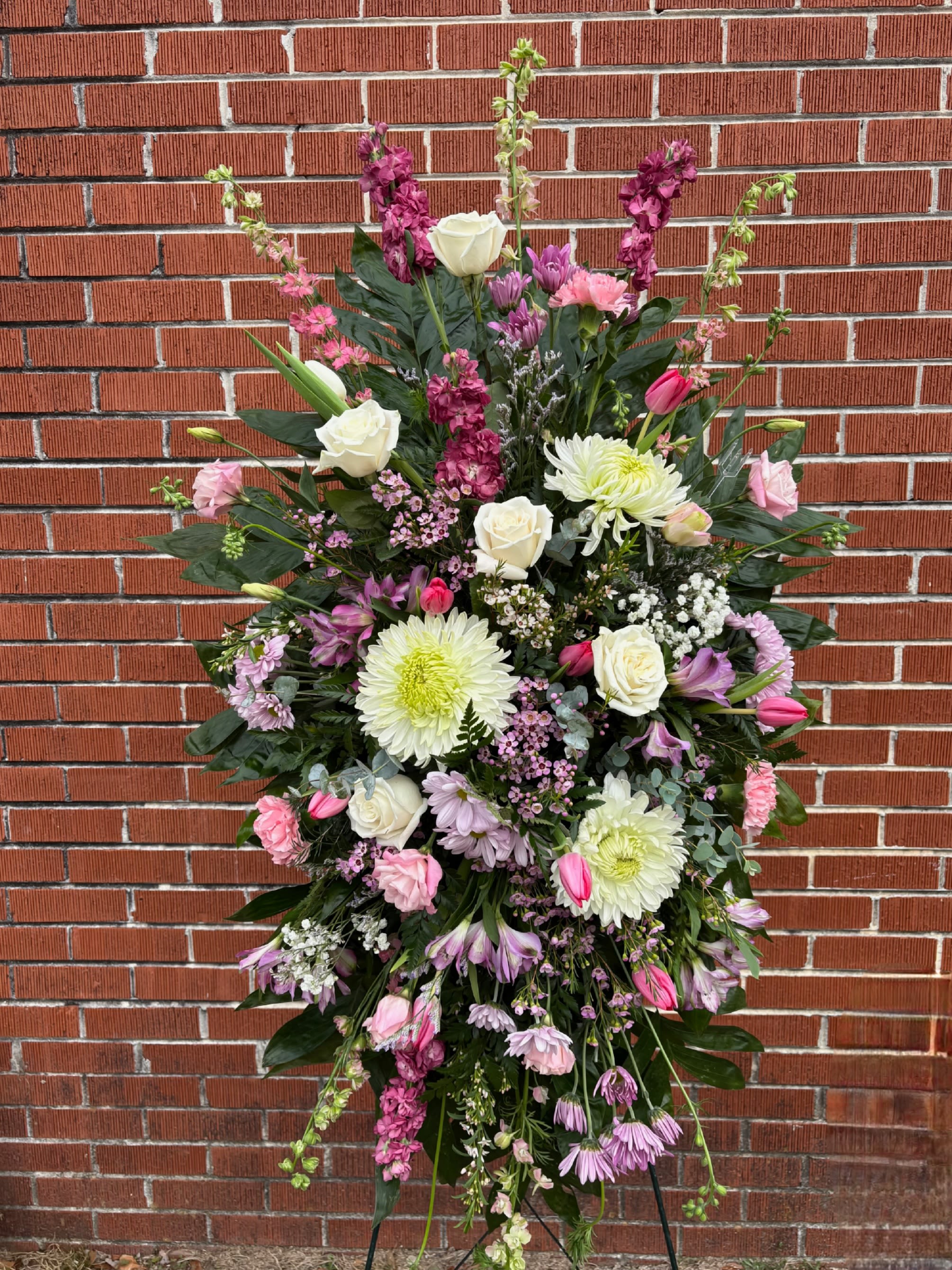 Tall standing spray of white, pink, and lavender flowers displayed on an easel.