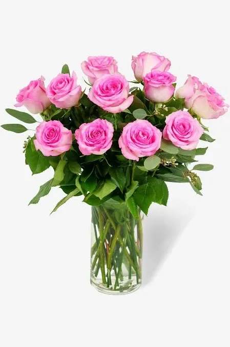 Dozen Pink Roses for Mom - A tall cluster of a dozen pink roses creates an elegant, romantic centerpiece that makes Mom feel truly cherished - perfect as a birthday bouquet or a "just because" surprise. The arrangement reads as both celebratory and intimate, so it also works beautifully for anniversaries, weddings, thank-you gestures, and Valentine's Day when you want to express love and appreciation.  Each bouquet features twelve long-stem pink roses in shades from soft blush to lively fuchsia, paired with airy white filler blooms and abundant green foliage for a fresh, classic contrast. Stems are arranged upright in a clear glass vase so the full, rounded heads and visible stems present a straightforward, garden-fresh look.   For Mom, this is the kind of bouquet that says she's seen and adored - a thoughtful way to mark a birthday, say thank you, or bring a romantic touch to any day. Delivered ready to display in the included vase; to keep blooms fresh, change the water every few days and trim stems slightly when you refresh the arrangement.