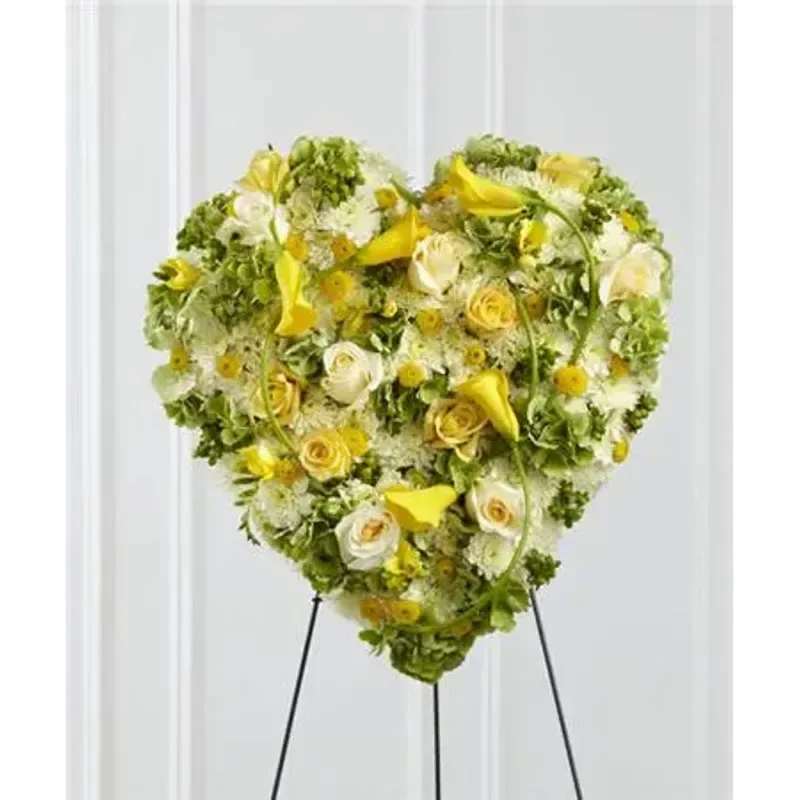 FTD® Glowing Ray Standing Heart™ - A collection of sunlit blooms, including, yellow roses, freesia, mini calla lilies, and button poms are accented with green hydrangea, white chrysanthemums, cream roses and green hypericum berries to form a sophisticated heart-shaped arrangement that offers a bright and elegant expression of caring kindness for their final goodbye. Displayed on a wire easel. 