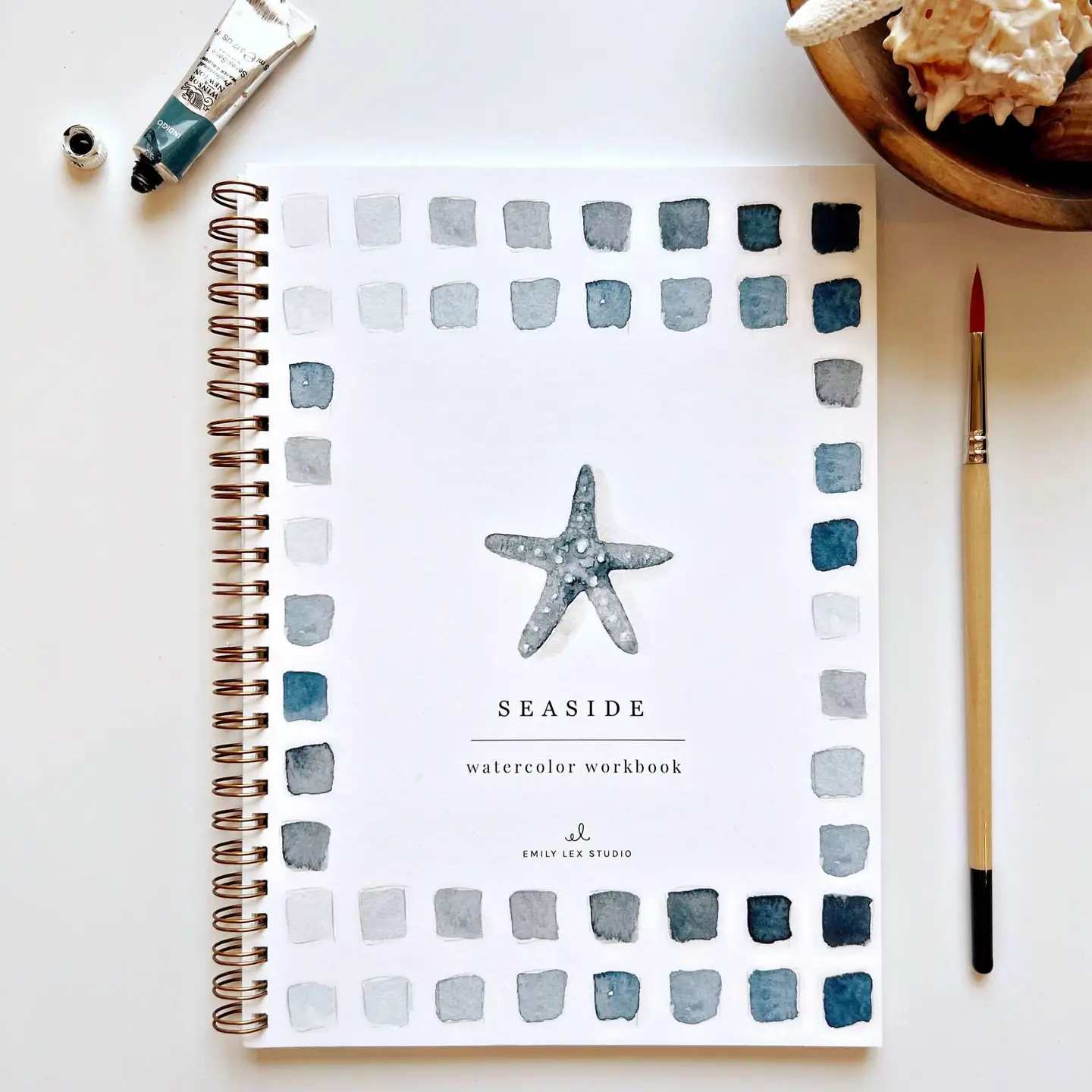 Watercolor workbook with a starfish cover and paintbrush beside it