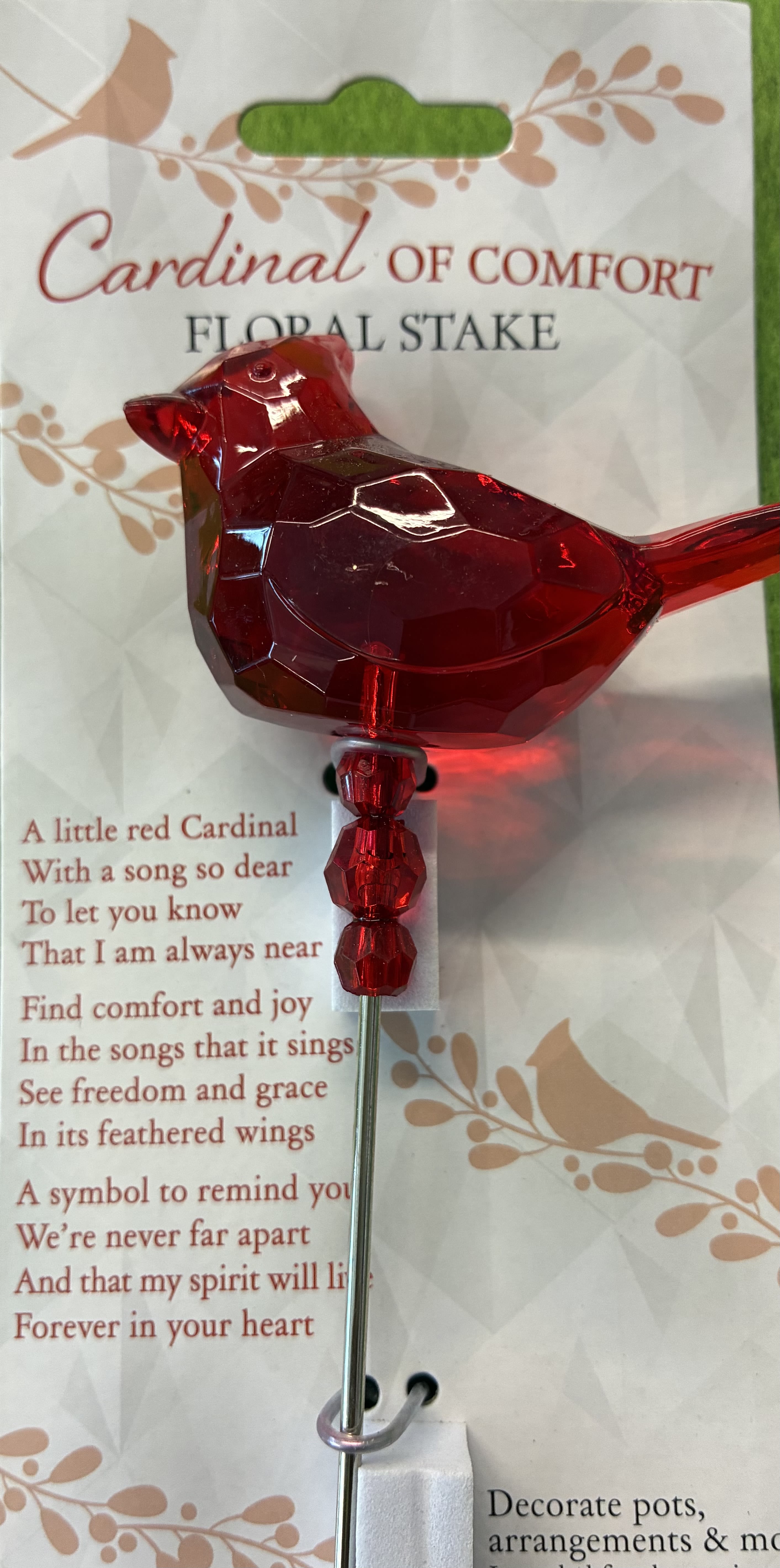Cardinal Stake - A translucent red cardinal figurine on a slim metal stake offers a tender, remembrance-focused accent perfect for sympathy arrangements or a keepsake gift for someone grieving. This decorative cardinal stake reads as a comforting symbol-the kind of small, luminous presence that lets the person you're thinking of know they are remembered and loved, whether tucked into a memorial pot, floral tribute, or garden display.  The cardinal has a glossy, faceted, glass-like finish that catches the light and draws the eye; it's mounted on a sturdy metal rod and arrives in printed retail packaging that includes a short, memorial-style poem and soft botanical graphics. The piece is compact and gift-ready, sized to insert into potted plants, burial urns, or mixed bouquets as a lasting accent rather than a fresh-flower product.  Made to be a thoughtful keepsake, this decorative stake works well for sympathy, memorials, or as a gentle token for someone missing a loved one-she'll see the bright red bird and feel genuinely comforted. Packaging is printed with the poem and intended for direct gifting; care is simple-place in soil, foam, or an arrangement where it can catch sunlight and continue to shine.