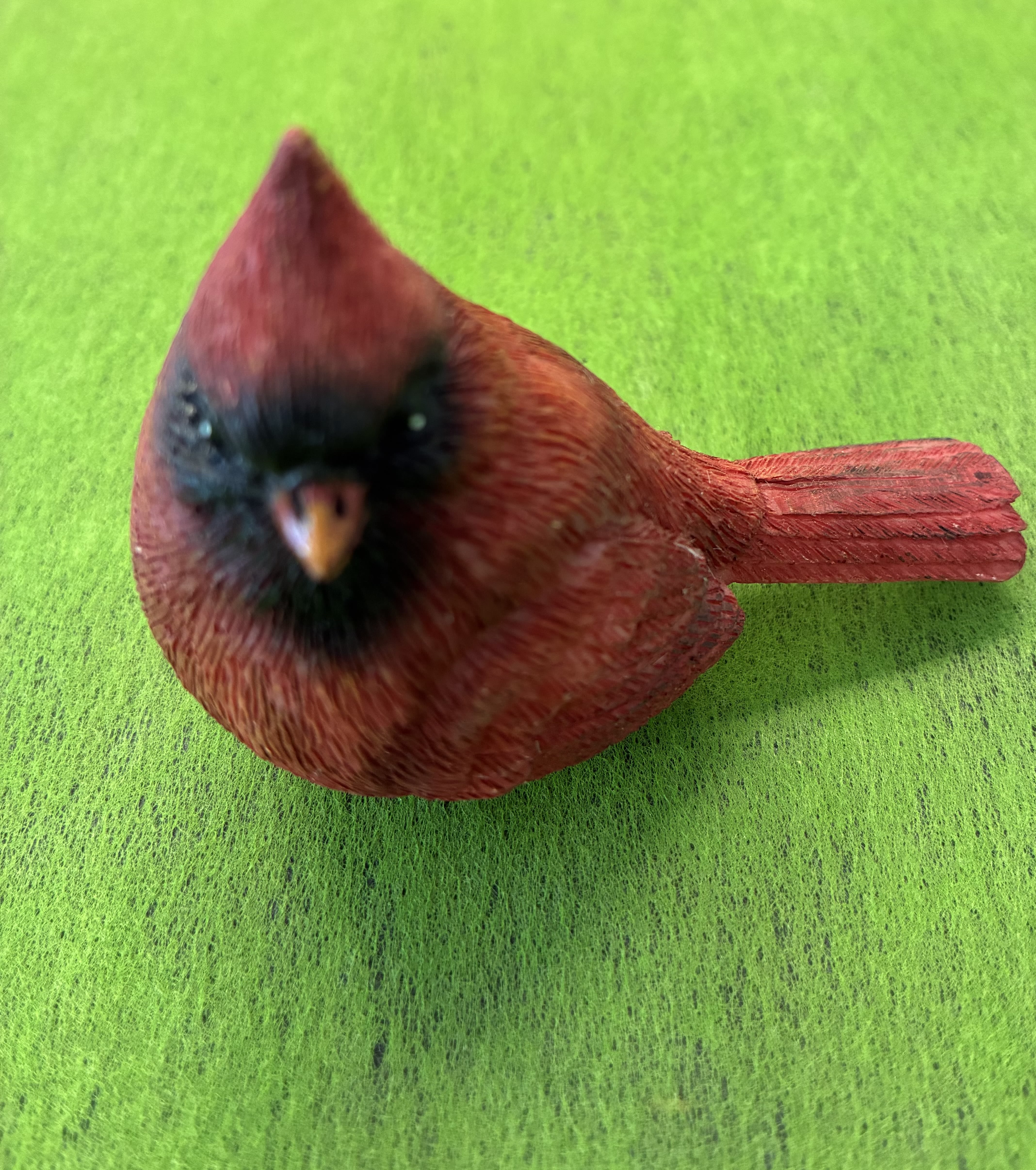 Cardinal Figurine - A bright red cardinal figurine makes an immediate, cheerful focal point for holiday décor or a nature-themed gift-perfect as a small accent for winter displays, mantel arrangements, or a sympathy table where a thoughtful token is called for. As a decorative piece rather than a live bouquet, this compact figurine brings the familiar symbolism of the cardinal-warmth, remembrance, and seasonal cheer-to the person you're thinking of without taking up much space.  The piece features a textured, carved-look finish with a vivid red body, a contrasting black face mask, and a pointed crest set against a lively green background in images. Its rustic, hand-painted appearance pairs beautifully with evergreen sprigs, pinecones, or a simple vase of cut stems if you choose to incorporate it into a floral arrangement. Compact and easy to place, it's an understated way to make someone feel seen during the holidays, winter months, or any time you want to add a cozy, natural touch to a gift.