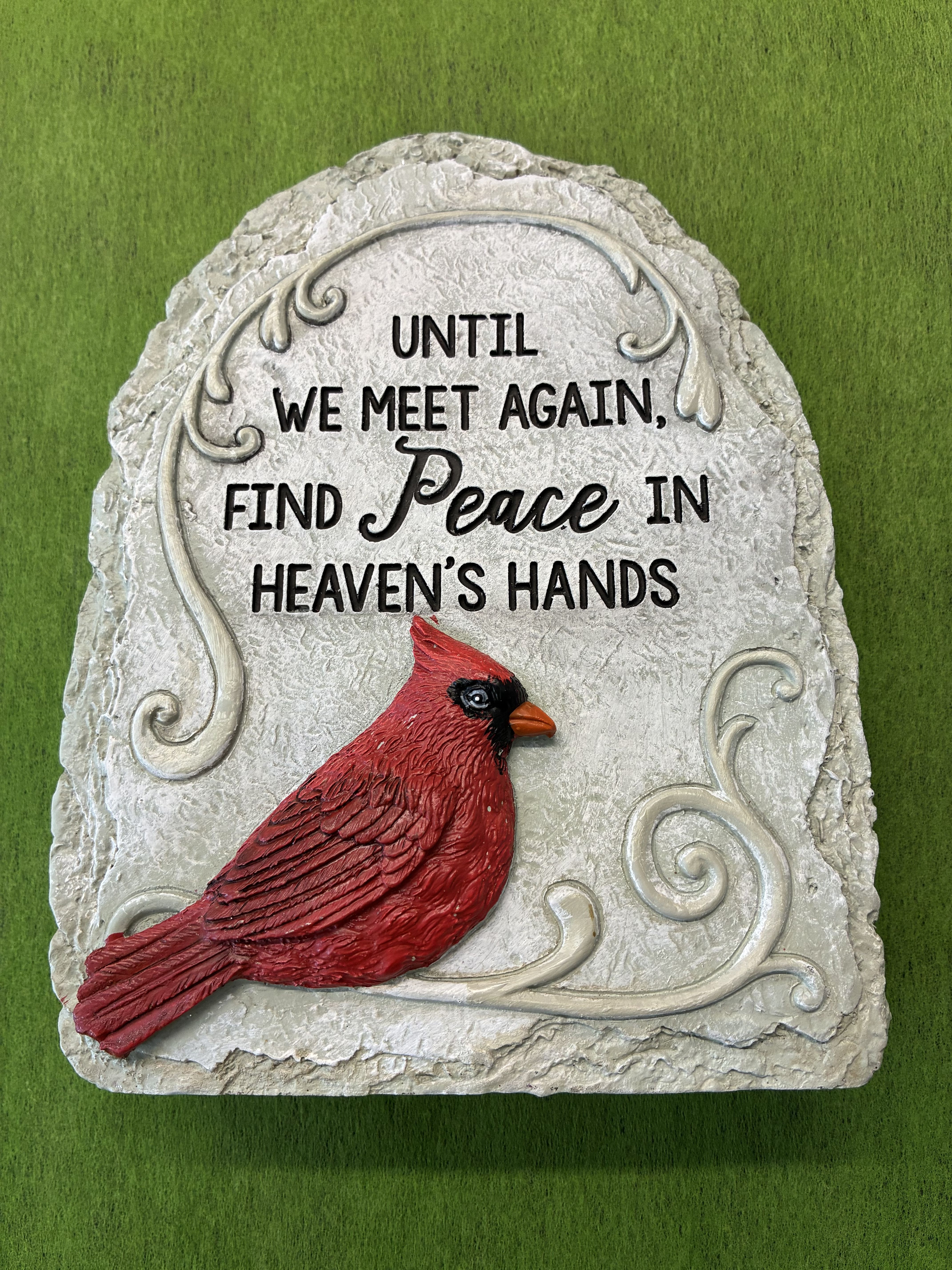 Cardinal Plaque - A bright red cardinal perched on a pale, textured memorial stone creates a quietly hopeful focal point for sympathy and remembrance. Perfect as a funeral accent or a graveside tribute, this memorial plaque - with its raised scrollwork border and centered inscription - reads "UNTIL WE MEET AGAIN, FIND Peace IN HEAVEN'S HANDS," offering a comforting message for someone grieving the loss of a loved one.  The plaque's light gray, rough-hewn surface highlights the vivid red of the cardinal and the crisp black lettering for strong visual contrast that holds up outdoors or on a mantel. Sized to be clearly readable without overwhelming a small space, it combines durable memorial stone with an elegant, handcrafted look. Place it at a gravesite, beside a favorite photo, or on a memorial table to let the recipient feel remembered and comforted; suitable for ordering now for sympathy, memorial services, or to send as a thoughtful keepsake.