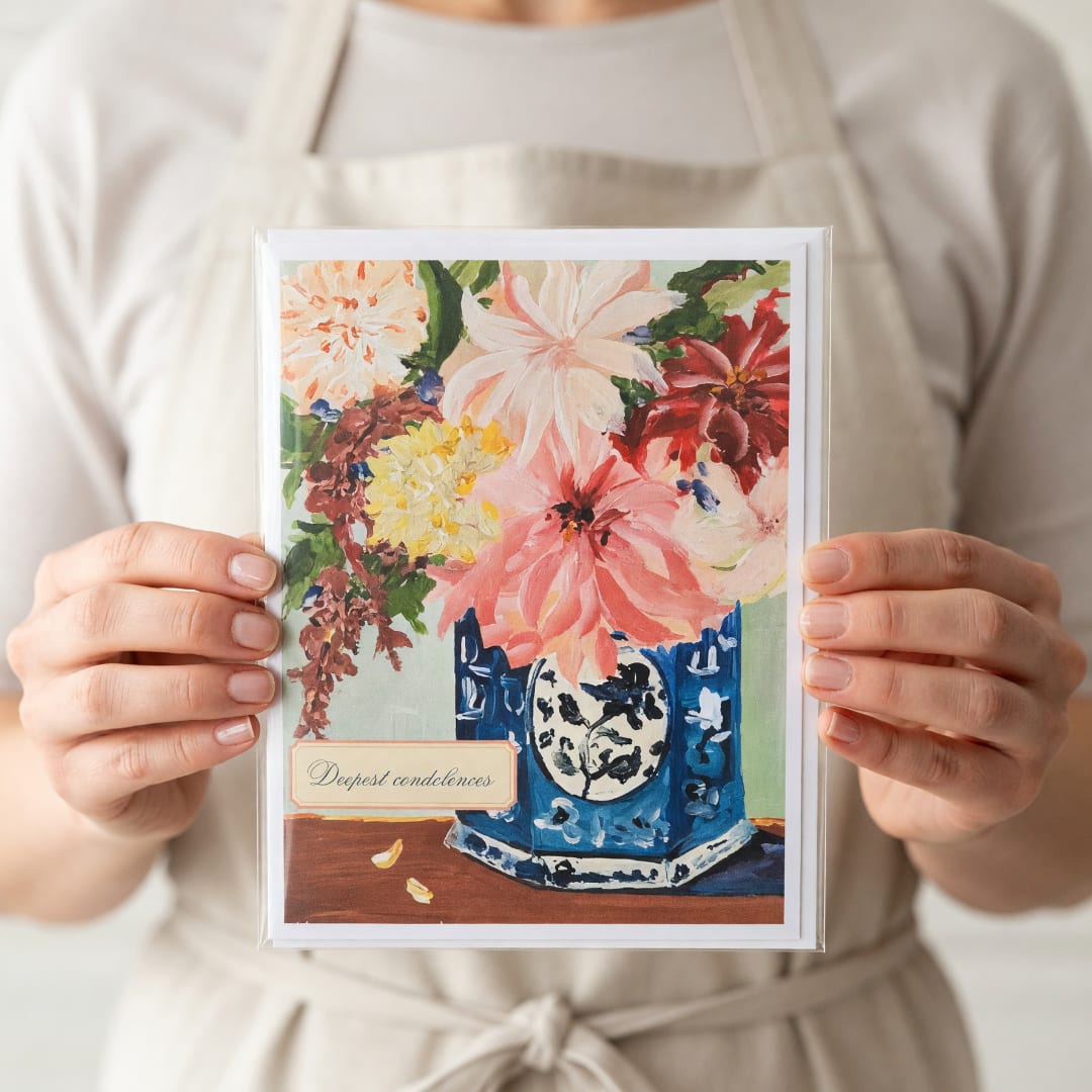 Person holding a condolence card with a floral painting and vase