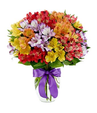 Colorful mixed bouquet in a clear glass vase with a purple ribbon