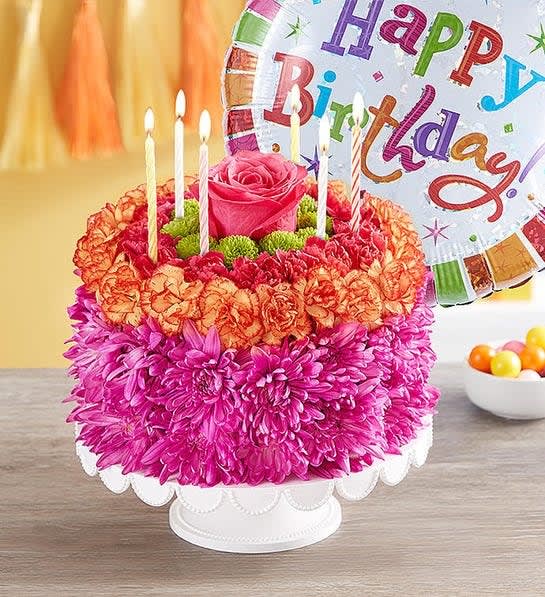 Birthday cake decorated with flowers and candles beside a birthday balloon