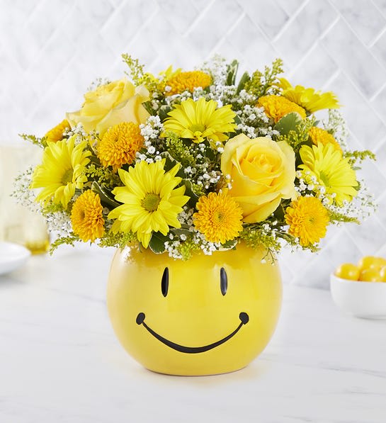 Yellow flower arrangement in a smiley-face ceramic pot