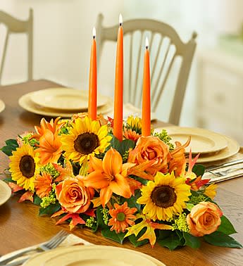 Orange floral centerpiece with sunflowers and roses around three tall candles