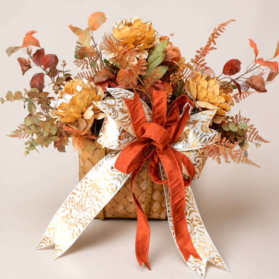 Autumn floral arrangement in a woven basket with orange ribbon and patterned bow