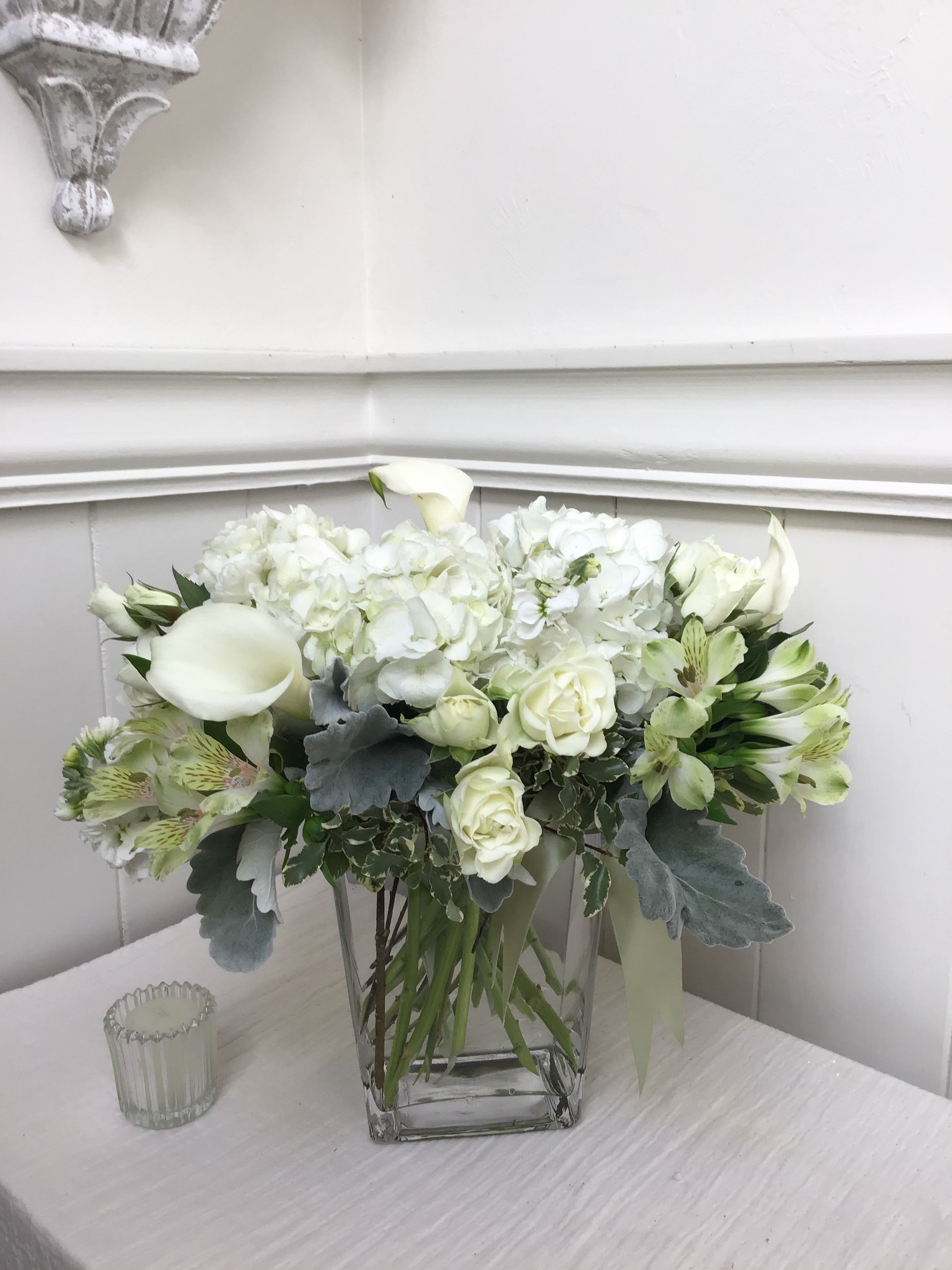 White floral arrangement in a clear square vase with calla lilies and roses