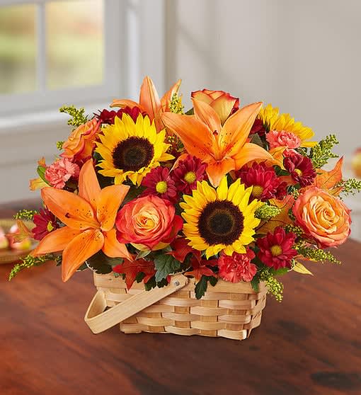 Bursting Fall Basket - Shades of golden yellow, warm orange and pops of rich red create a vibrant gift that lets them know they’re on your mind. Flowers like sunflowers, lilies, chrysanthemums and roses make up this vivid fall basket. Arranged in a 7" basket.