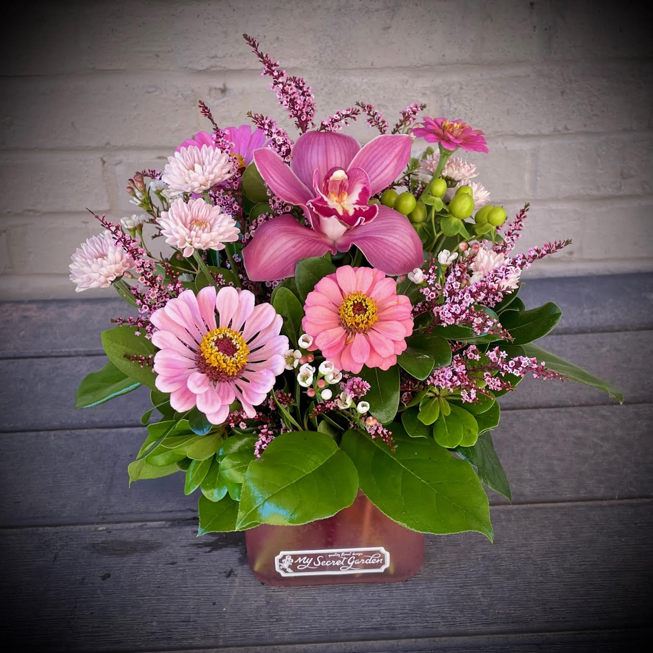 Pink orchid and daisy arrangement in a square container