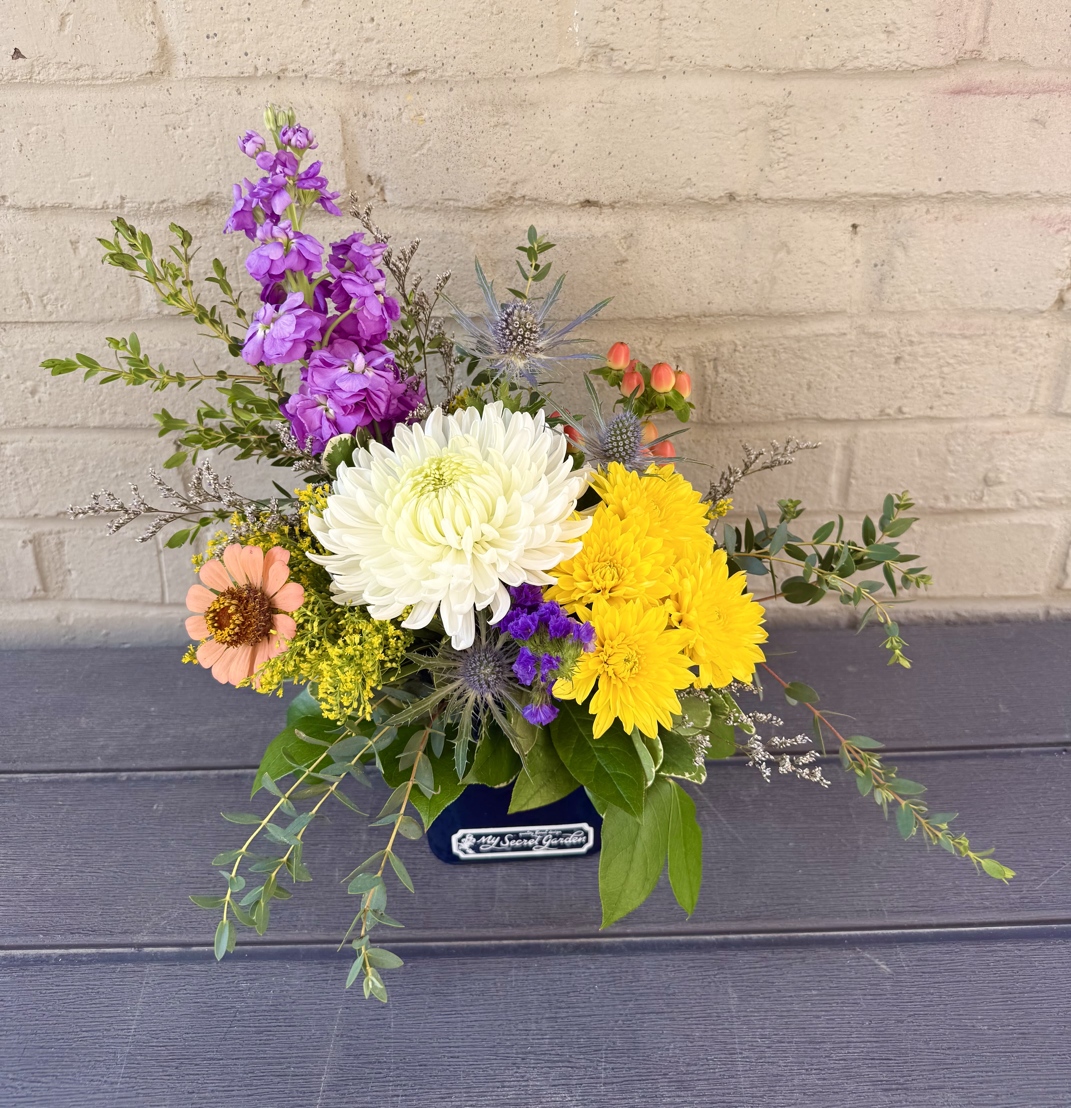 Brilliant Blossoms  - "Brilliant Blossoms" is a beautiful and petite floral design of vibrant flowers such as Chrysanthemums, Stock, Gomphrena, and an assortment of fillers to create a stunning and distinctive floral gift. Including colors of purple, orange , white and yellow, this lovely bouquet is sure to brighten any home or office space.