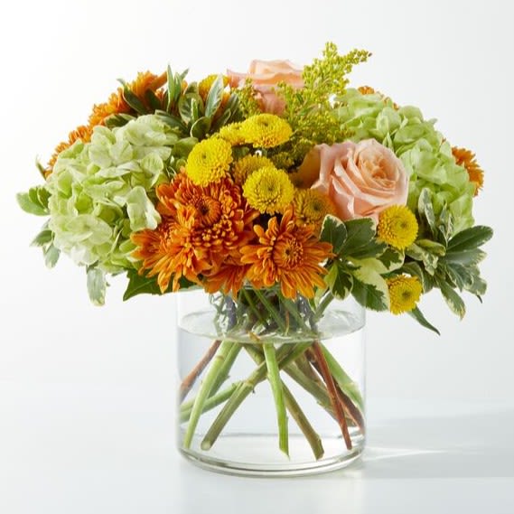 Orange and yellow flowers in a clear glass vase with pale pink roses