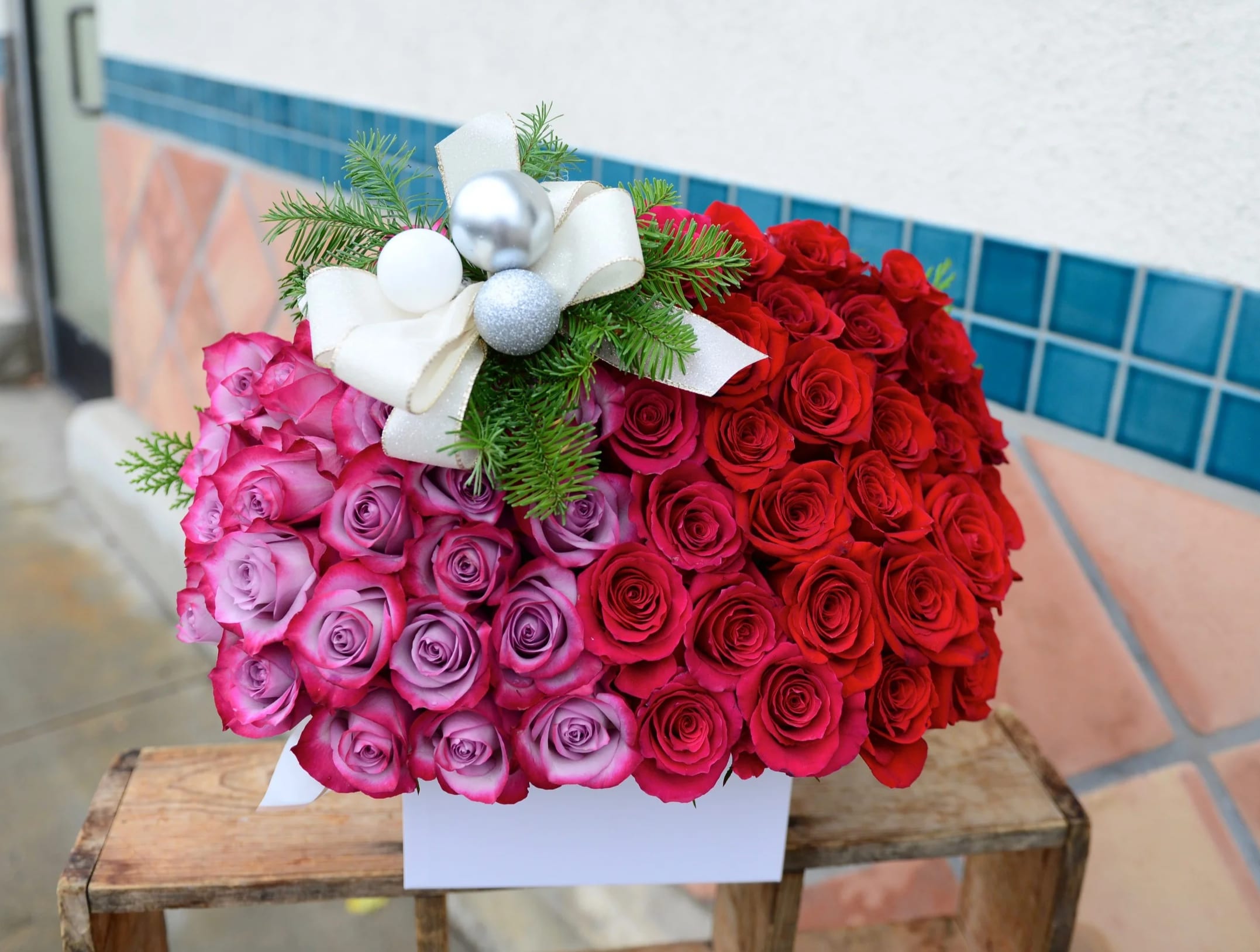 Heart-shaped bouquet of red and pink roses with a white ribbon bow