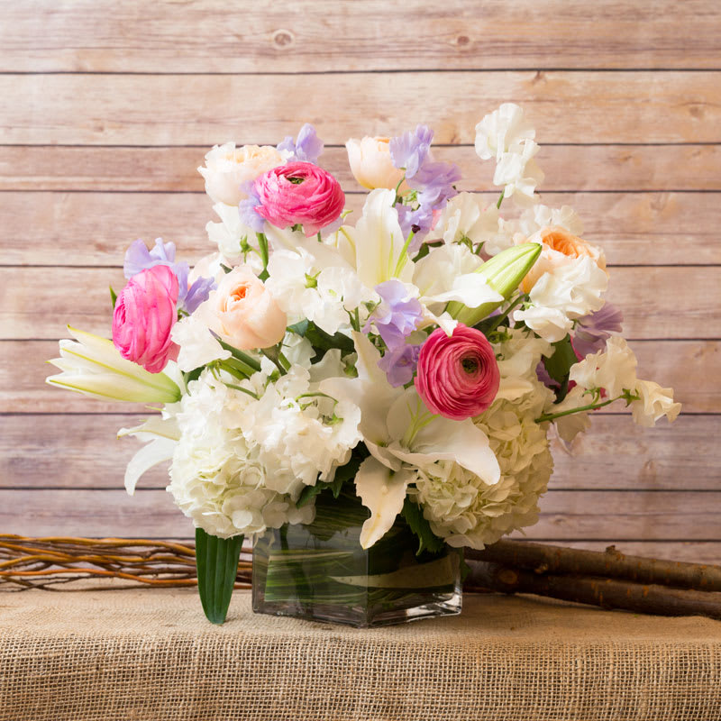 DELICATE ARRANGEMENT  - SOFT ARRANGEMENT IN GLASS CUBE, WITH WHITE HYDRANGEAS, WHITE LILIES, WHITE AND LAVENDER SWEET PEAS, PEACH ROSES, AND PINK RANANCULUS.