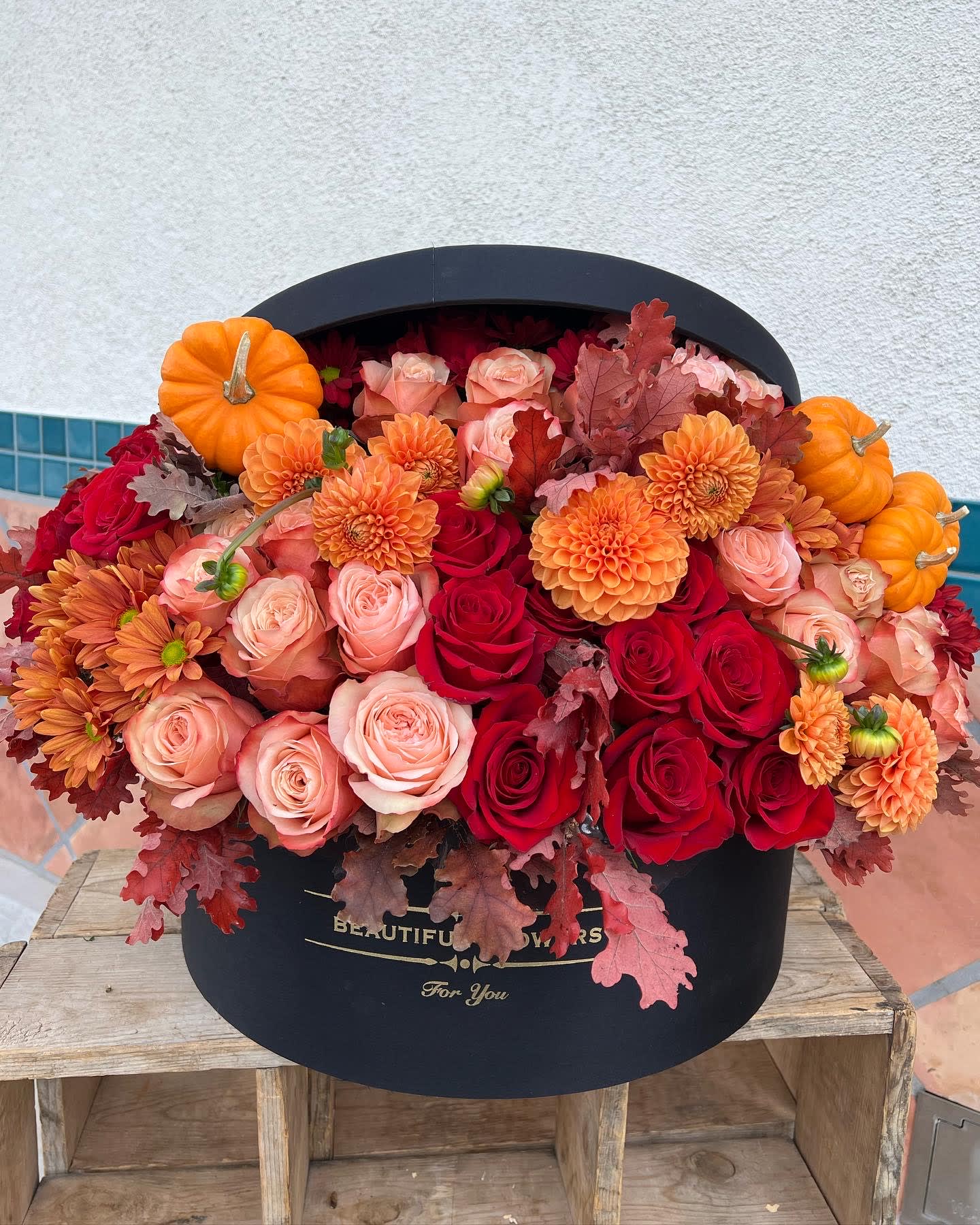 Orange pumpkins and red, peach, and orange flowers in a black hatbox
