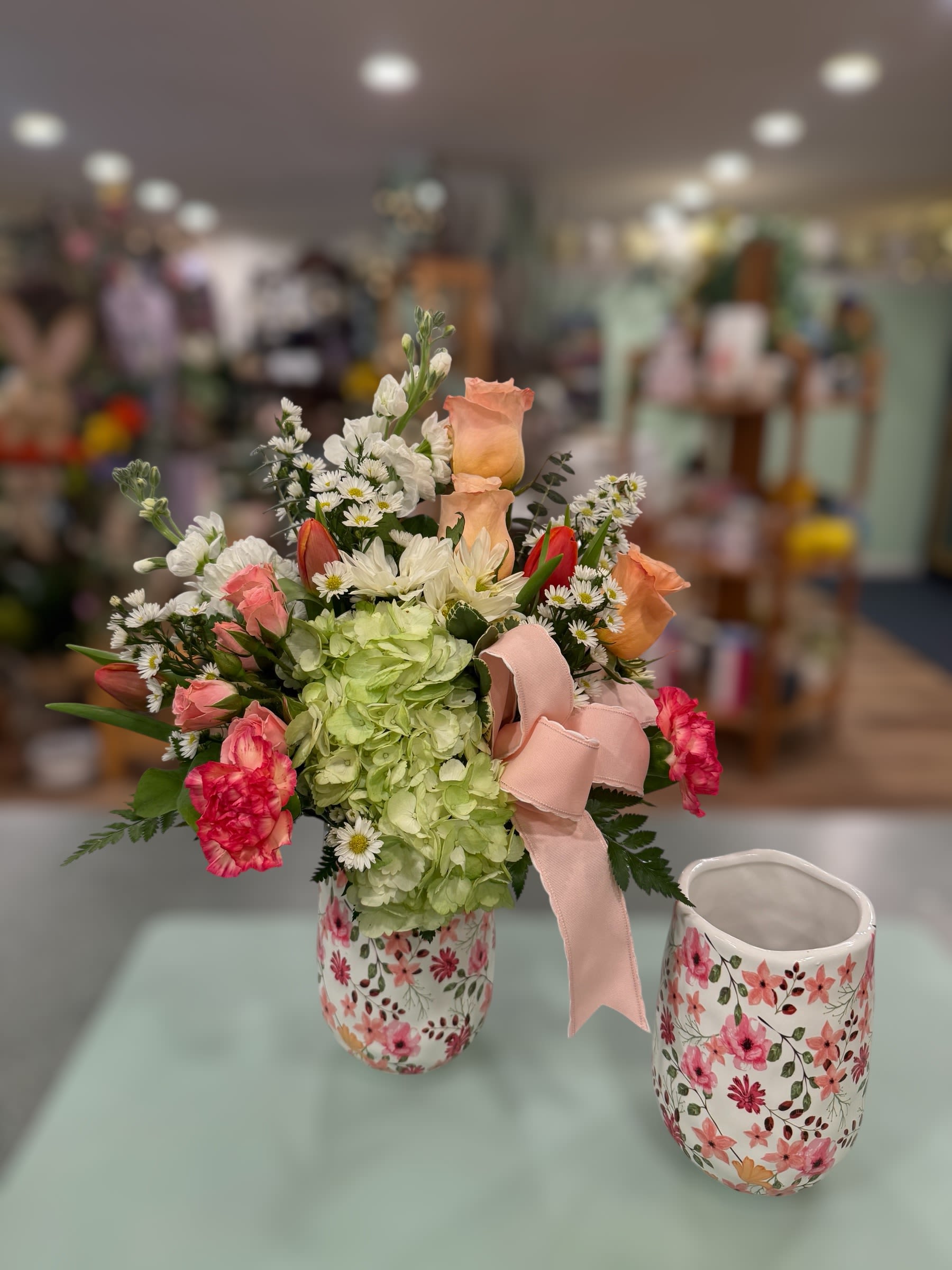 Spring Charm (SC) - A lush pale green hydrangea crown sets the tone for this spring bouquet.  Spring Charm is a garden-style flower arrangement perfect for birthdays, Mother's Day, or any spring celebration. The combination of peach and pink roses with bright pink carnations and delicate white daisy-like blooms creates a cheerful, romantic feel that makes the recipient feel warmly celebrated and truly seen.   ***Flower color/type may vary depending on availability. 