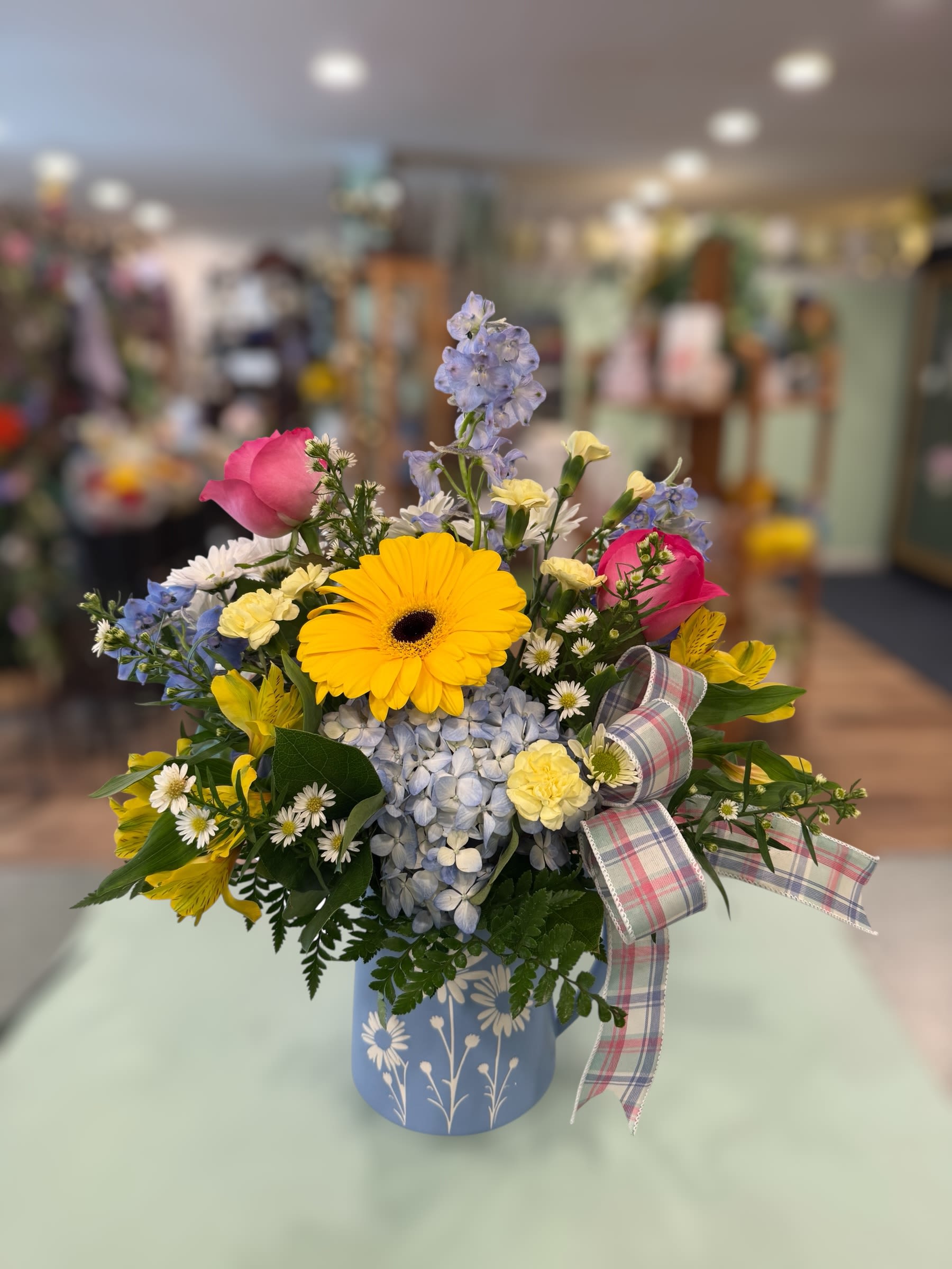 Daisy Bliss (DB) - This colorful arrangement is designed in a ceramic blue daisy pitcher with a bow. Perfect for all occasions!  ***Flower type/color may vary depending on availability.