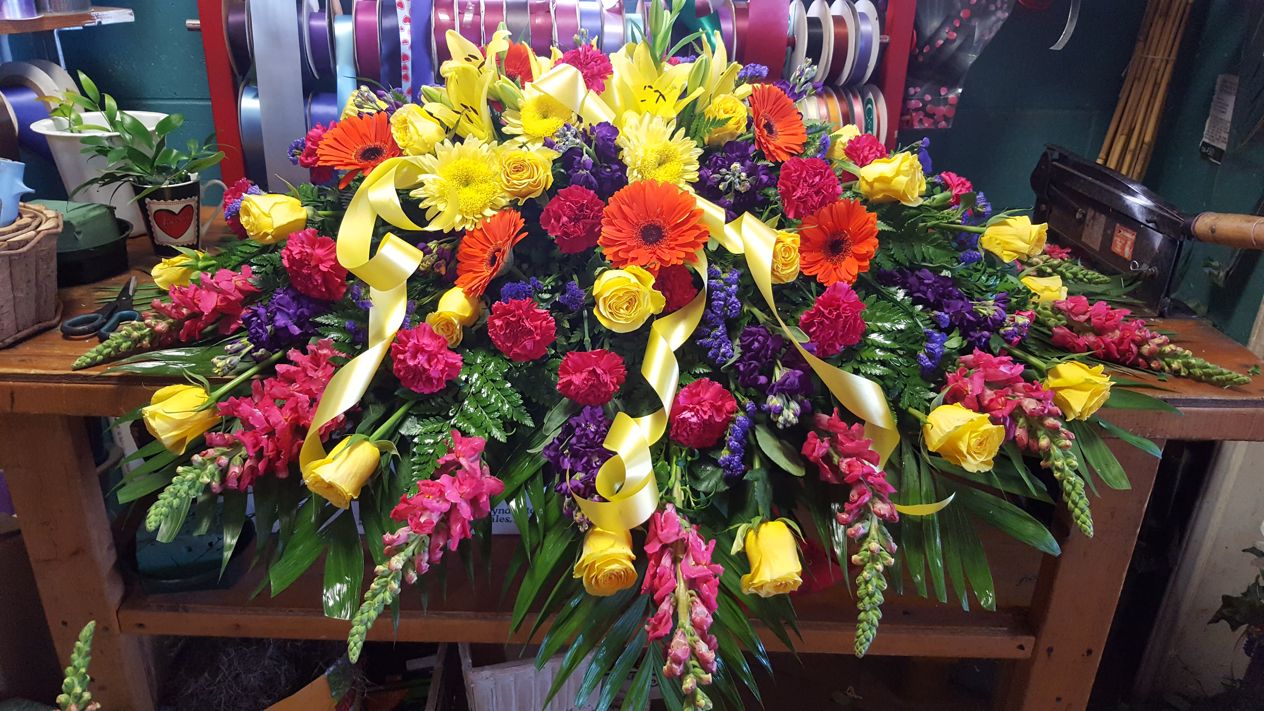 Large colorful floral casket spray with yellow, pink, purple, and orange blooms