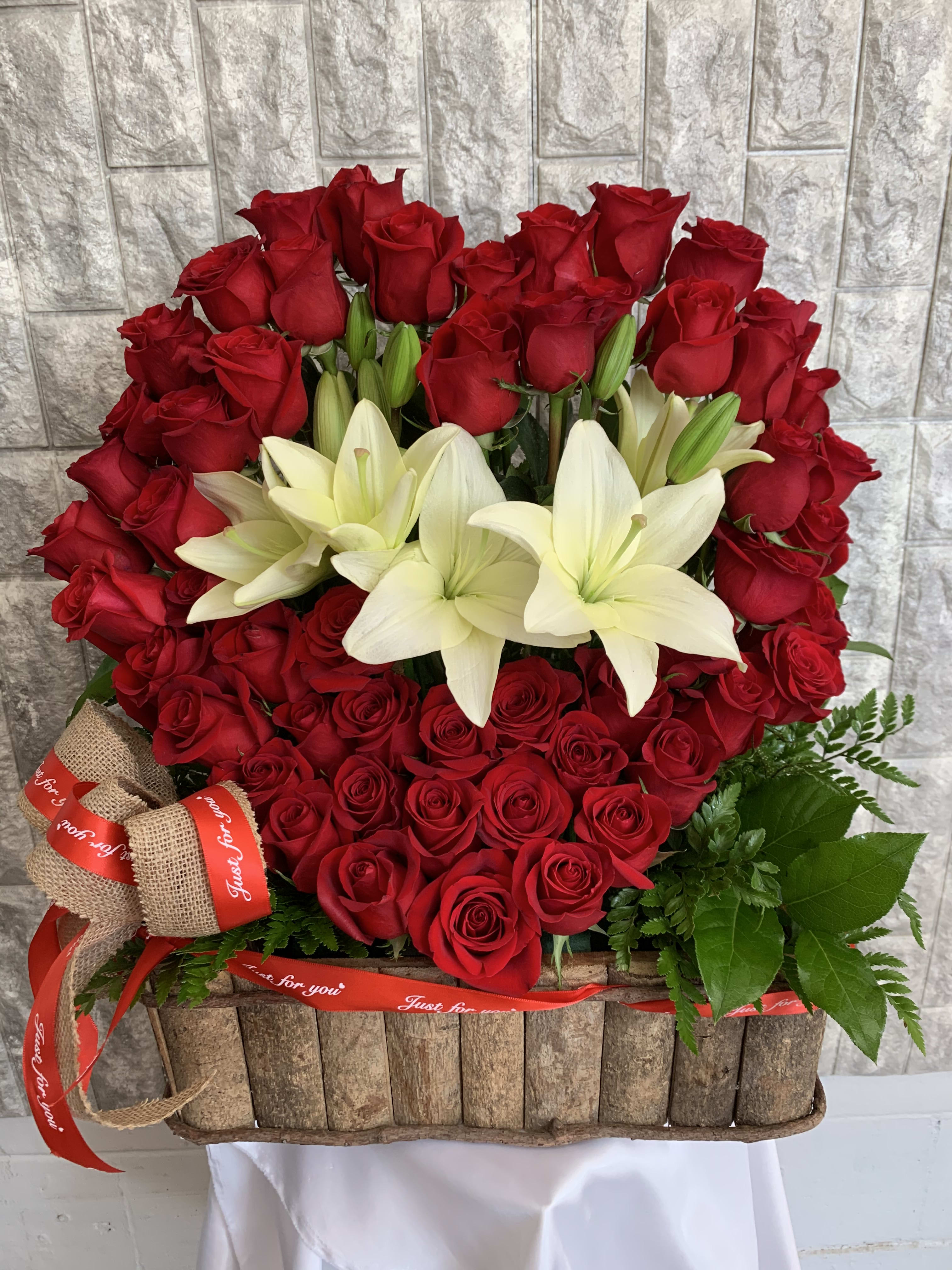 Red roses and white lilies arranged in a rustic basket with ribbon