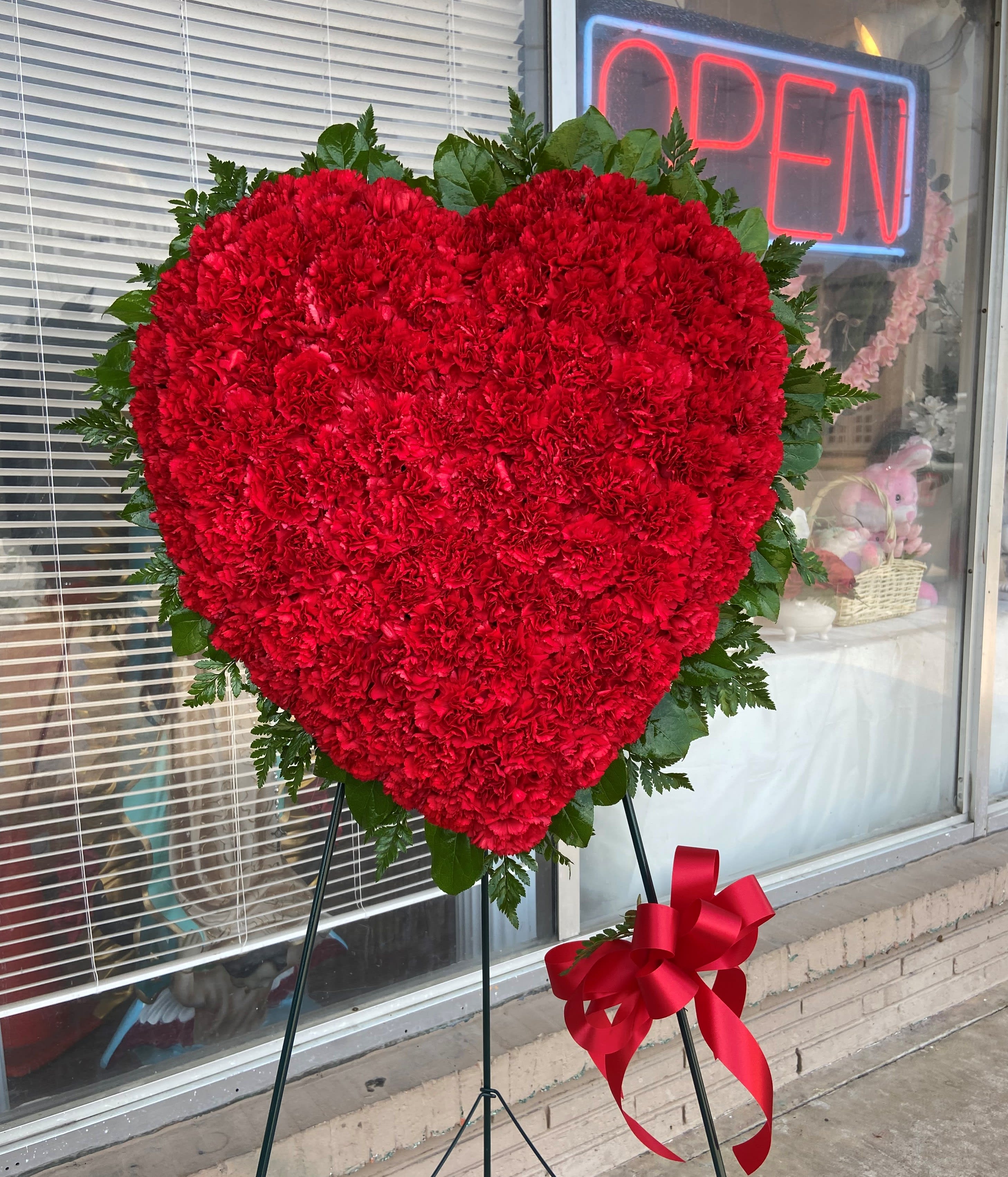 Heart-shaped red carnation standing spray with a ribbon on an easel