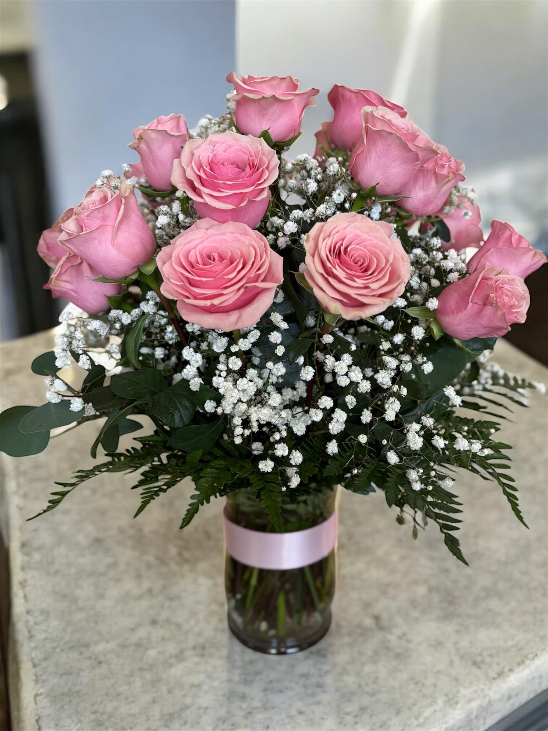 Pink roses and baby's breath in a glass vase with a pink ribbon