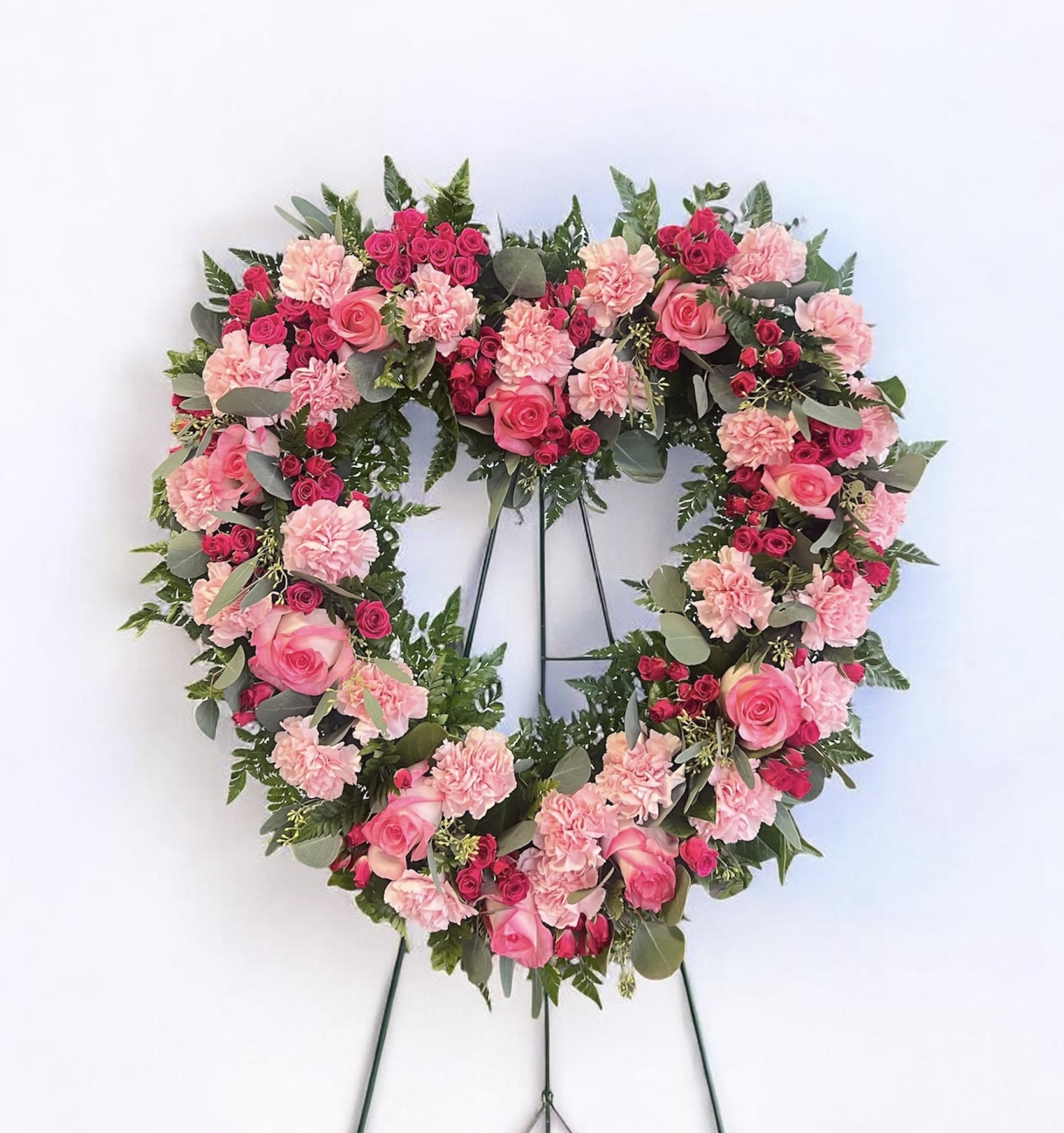 Heart-shaped floral wreath with pink roses and carnations on a stand