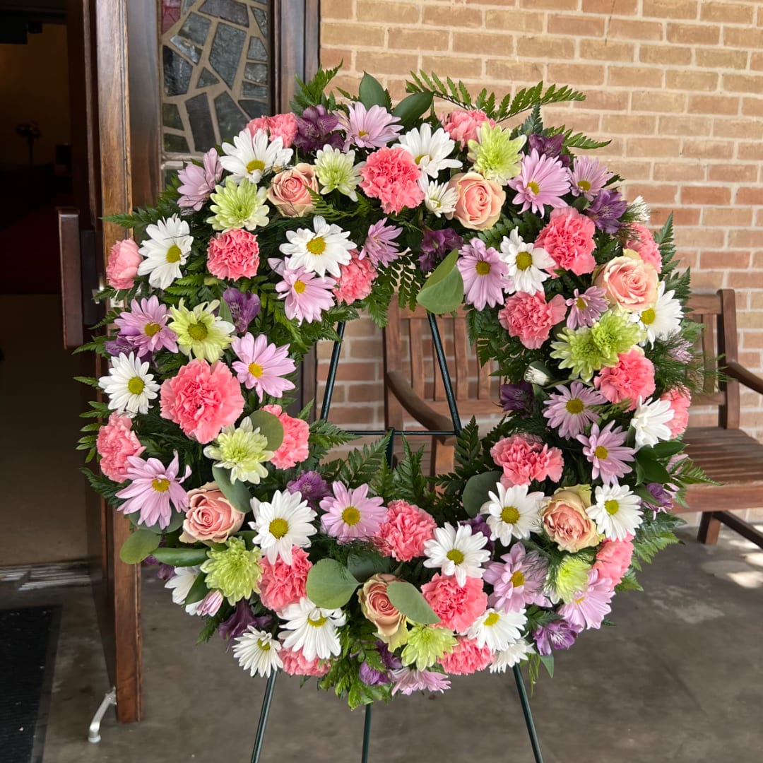 Round floral wreath with pink, white, purple, and green blooms on a stand