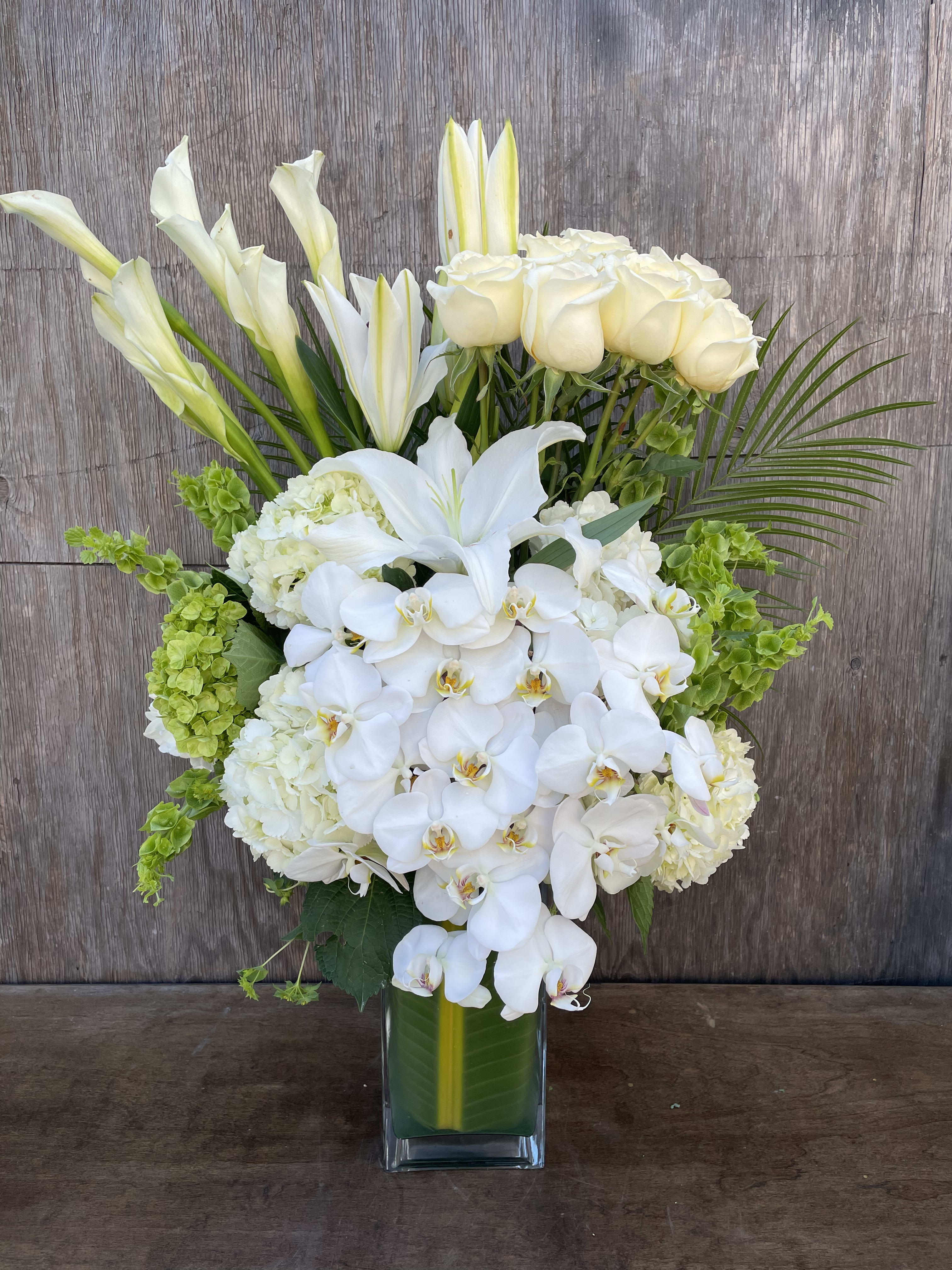 White orchids, roses, lilies, and green hydrangeas in a glass vase