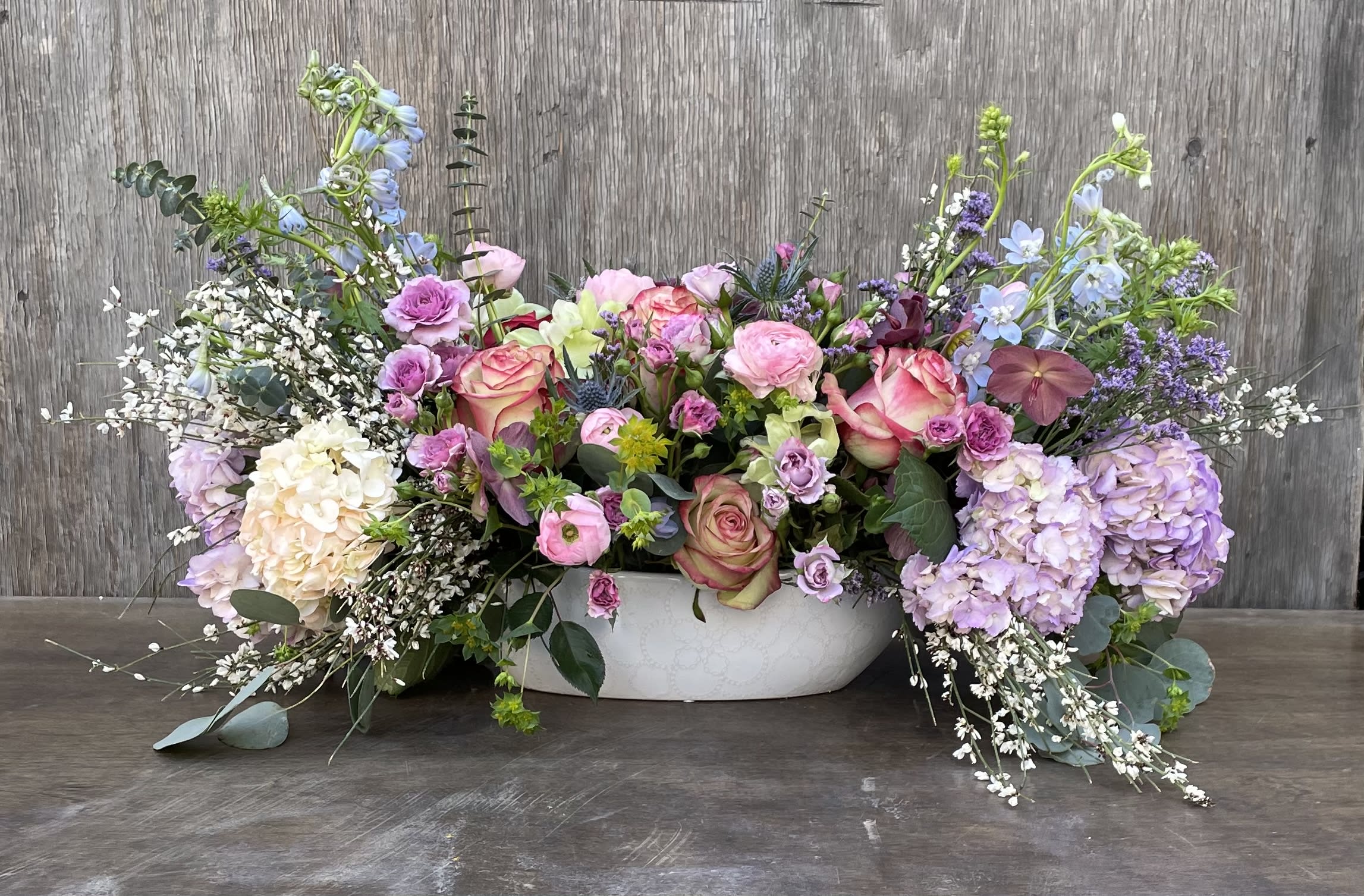Low floral centerpiece with pink roses, lavender hydrangeas, and blue delphinium in a white bowl