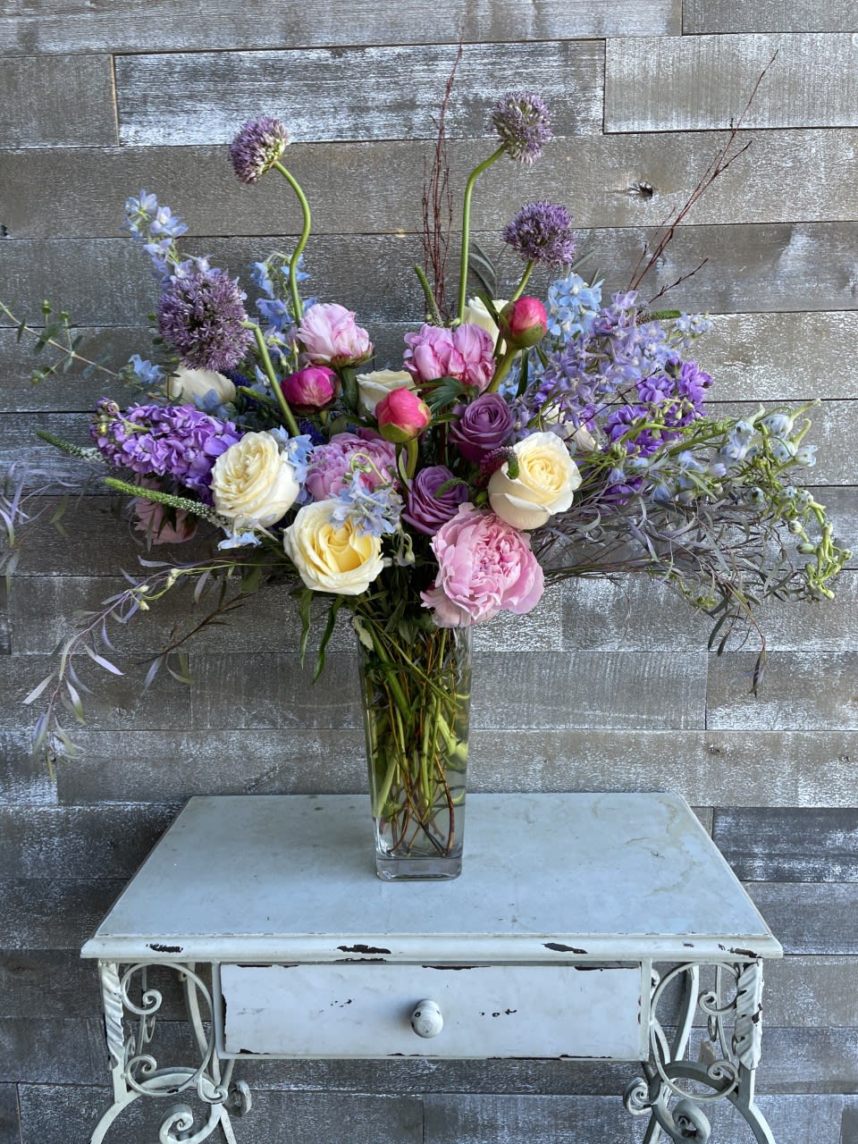 Tall mixed bouquet of pink, purple, and white flowers in a glass vase