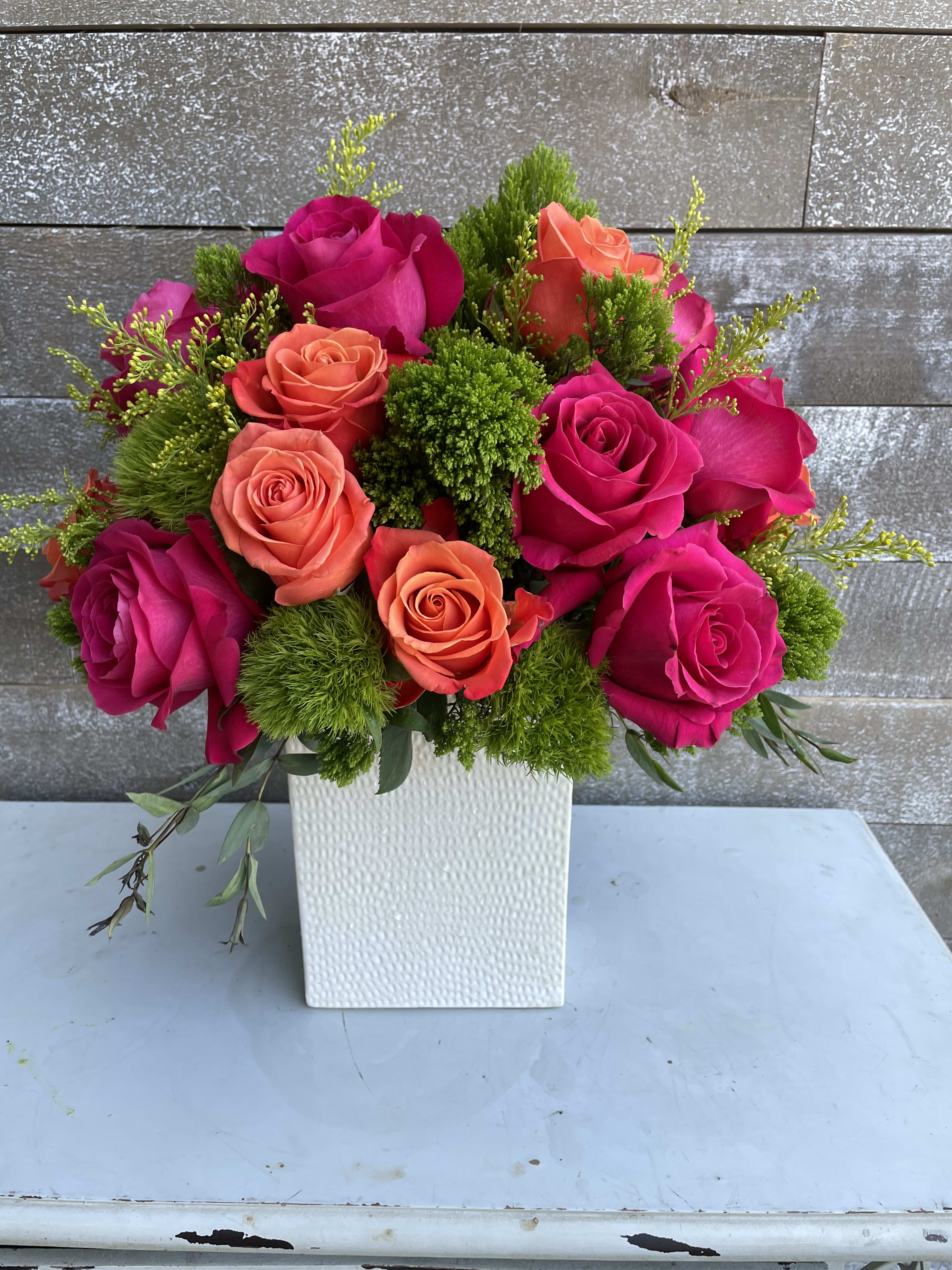 Pink and coral roses arranged in a white square vase