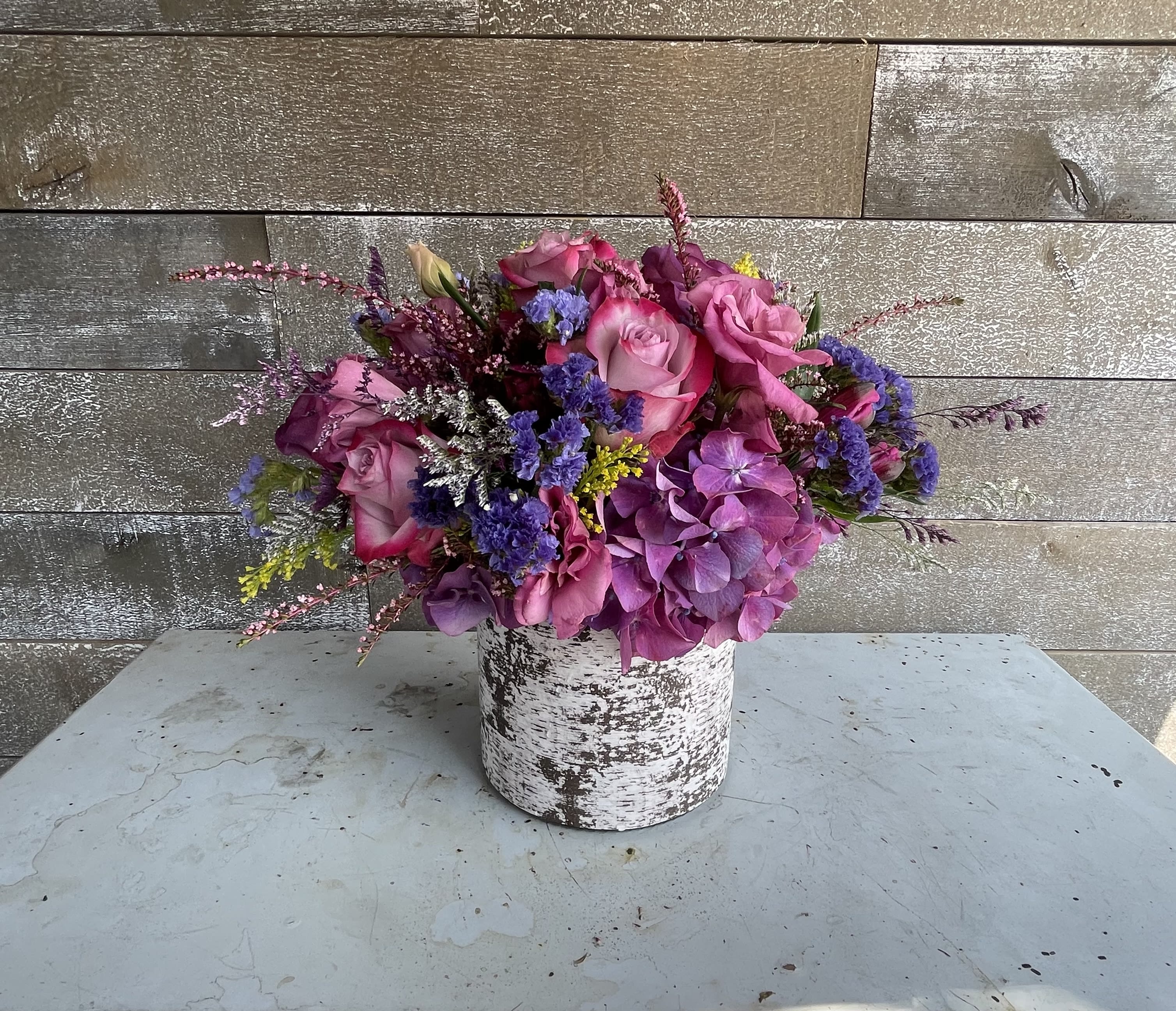 Pink and purple floral arrangement in a white textured container