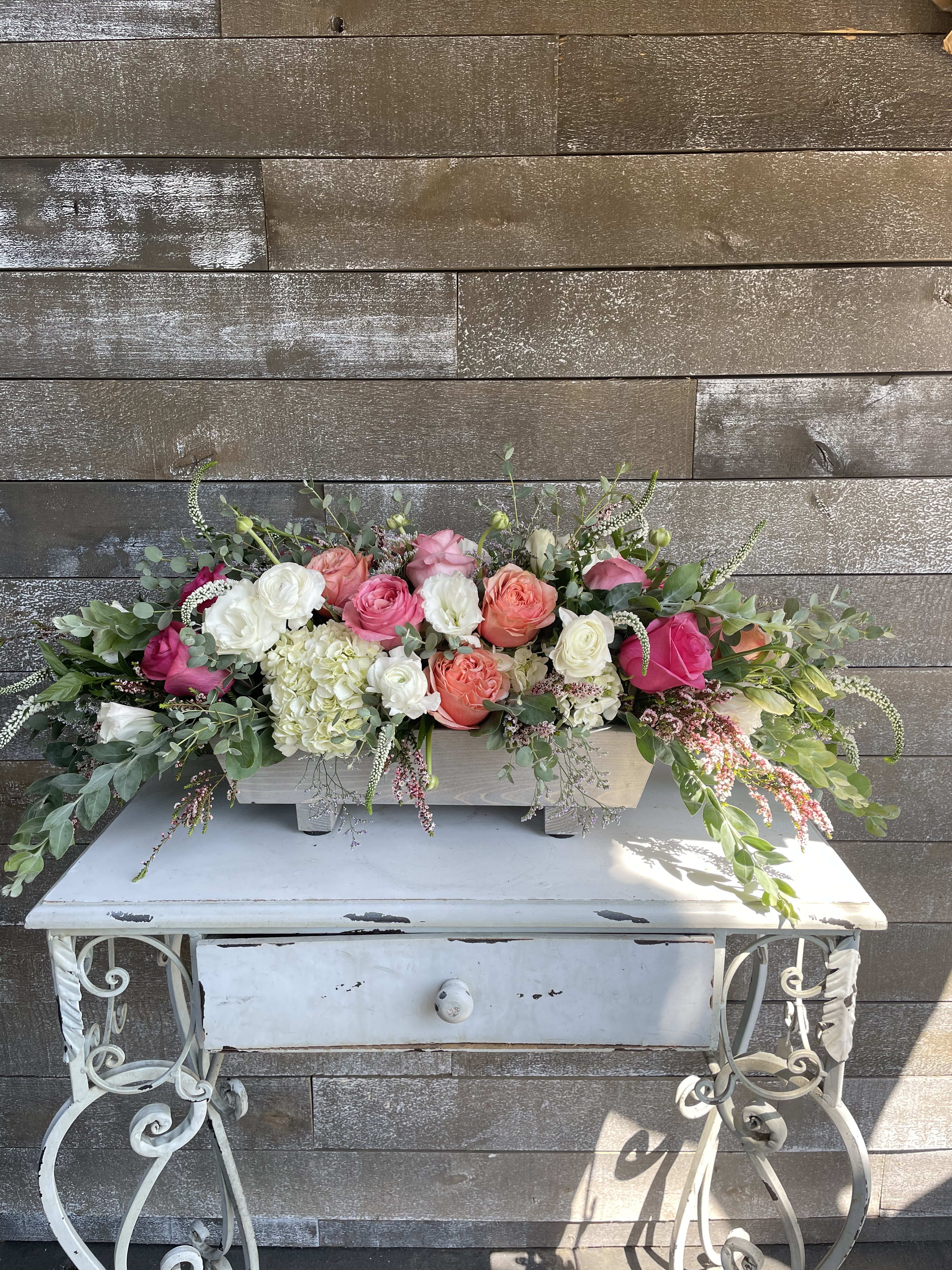 Long floral arrangement of pink, coral, and white roses in a white container
