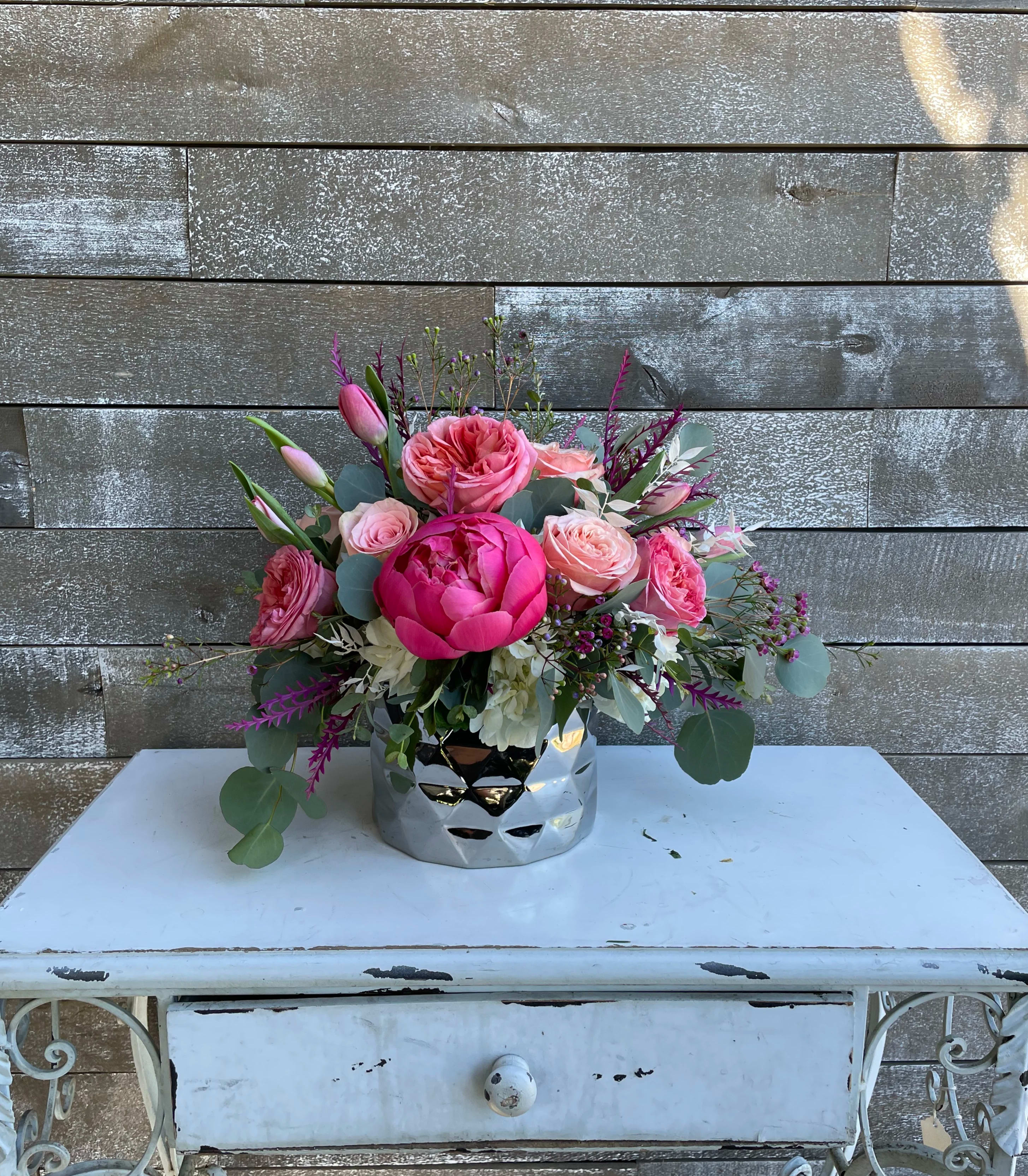 Pink floral arrangement in a silver vase on a white table