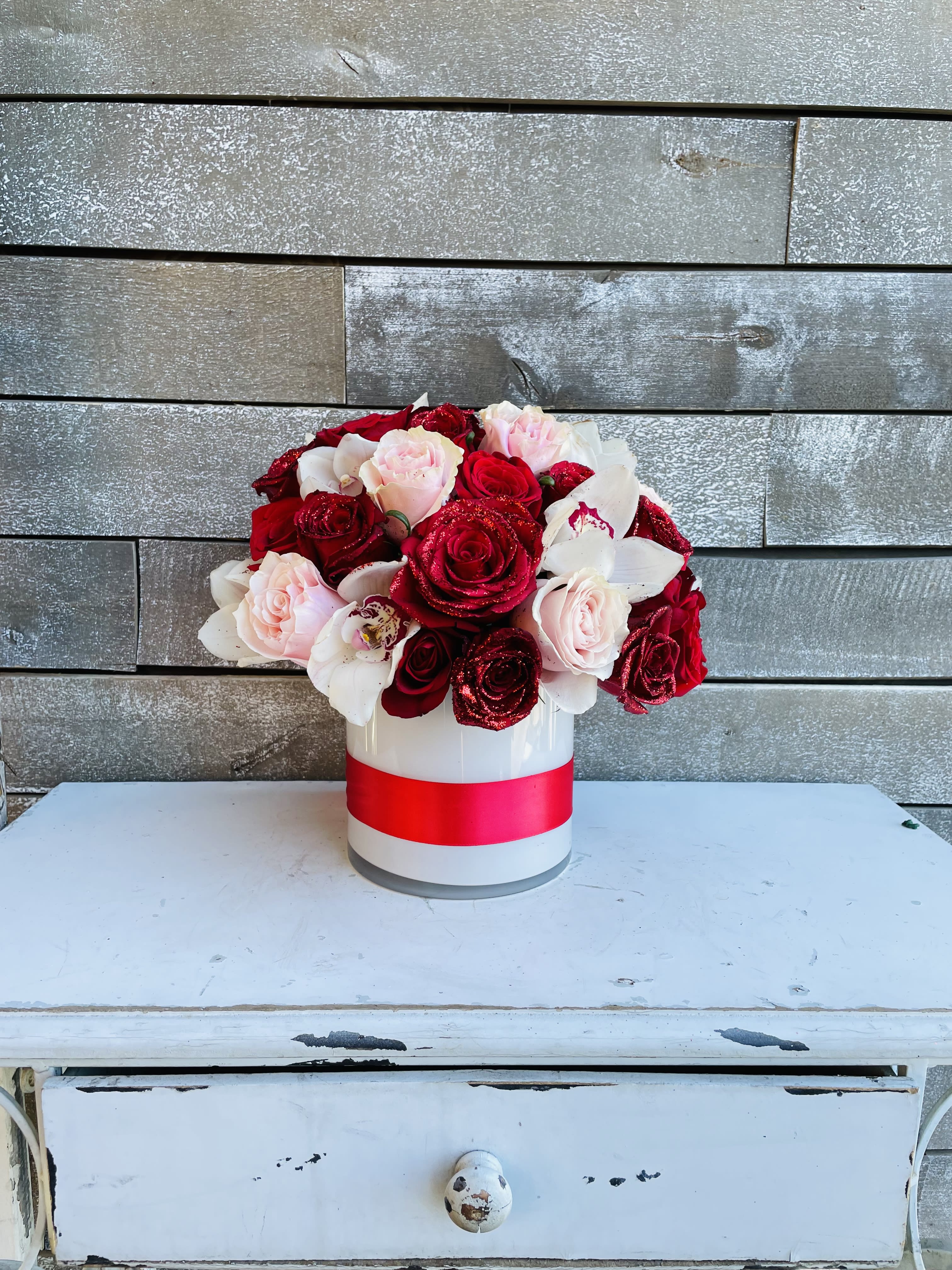 Red and blush roses arranged in a white hatbox with a pink ribbon
