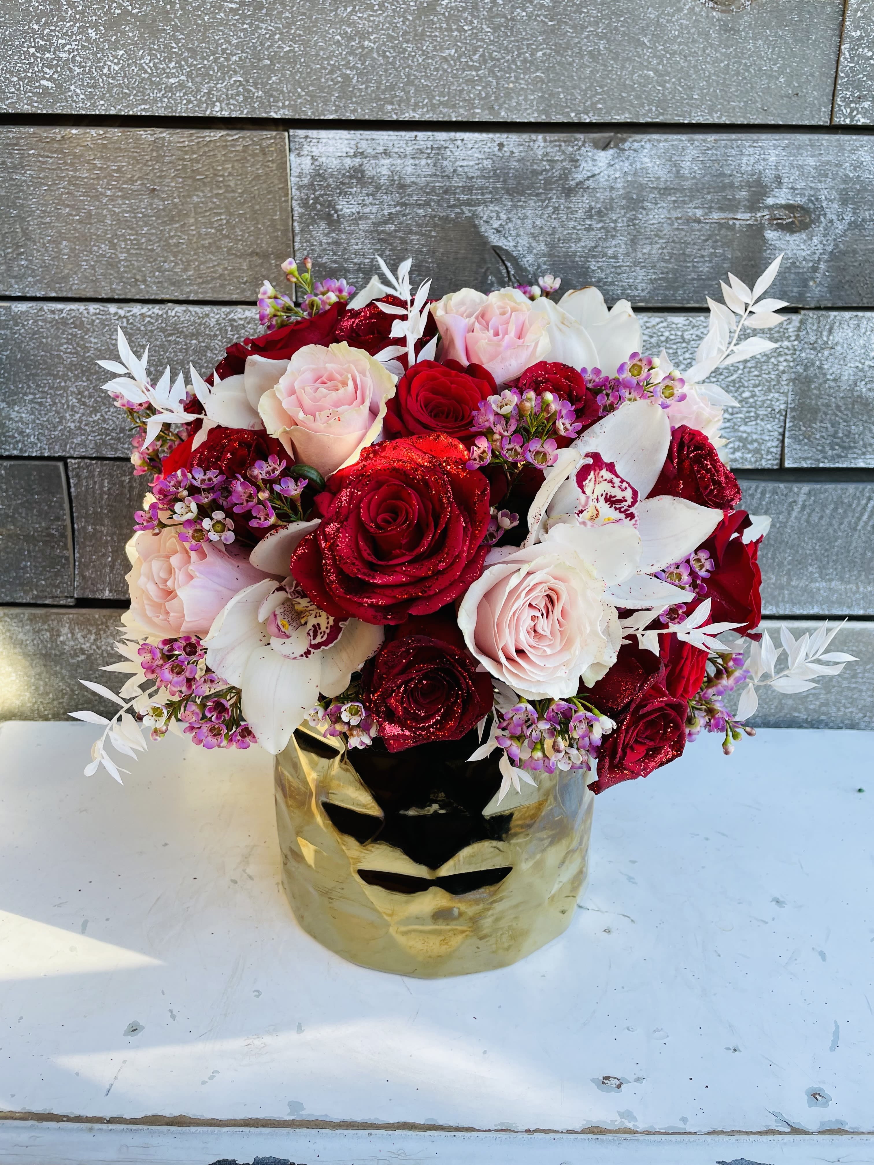 Bouquet of red and blush roses with white orchids in a gold mask vase