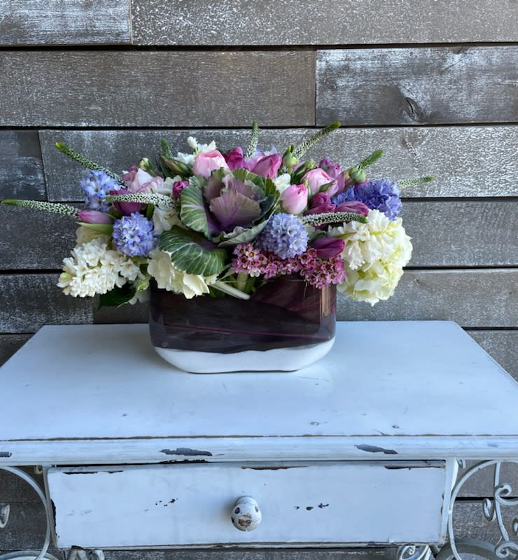 Mixed pink, purple, and white flower arrangement in a dark glass vase