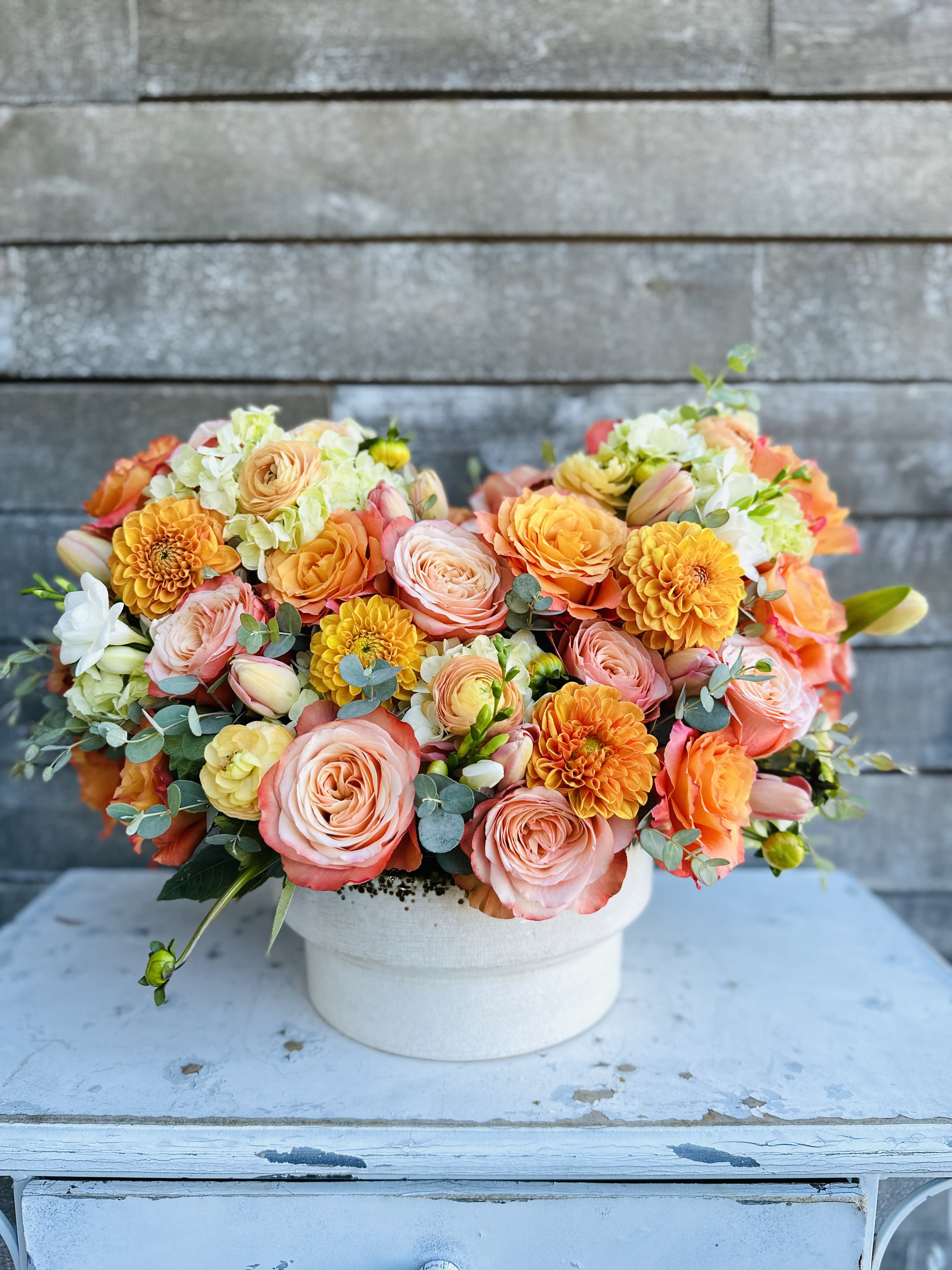 Peach and orange mixed flower arrangement in a white vase