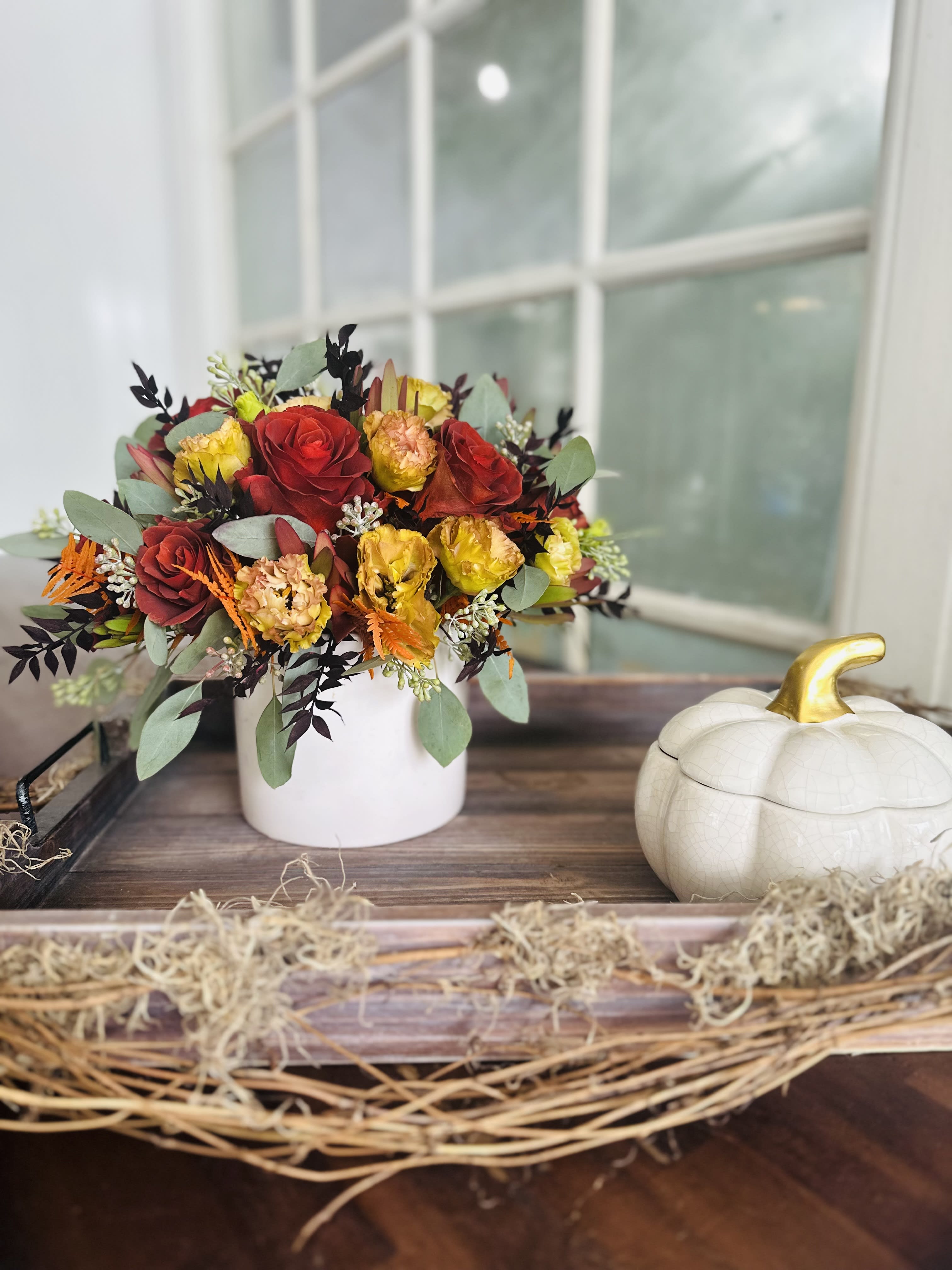 Red and yellow roses in a white vase beside a decorative pumpkin