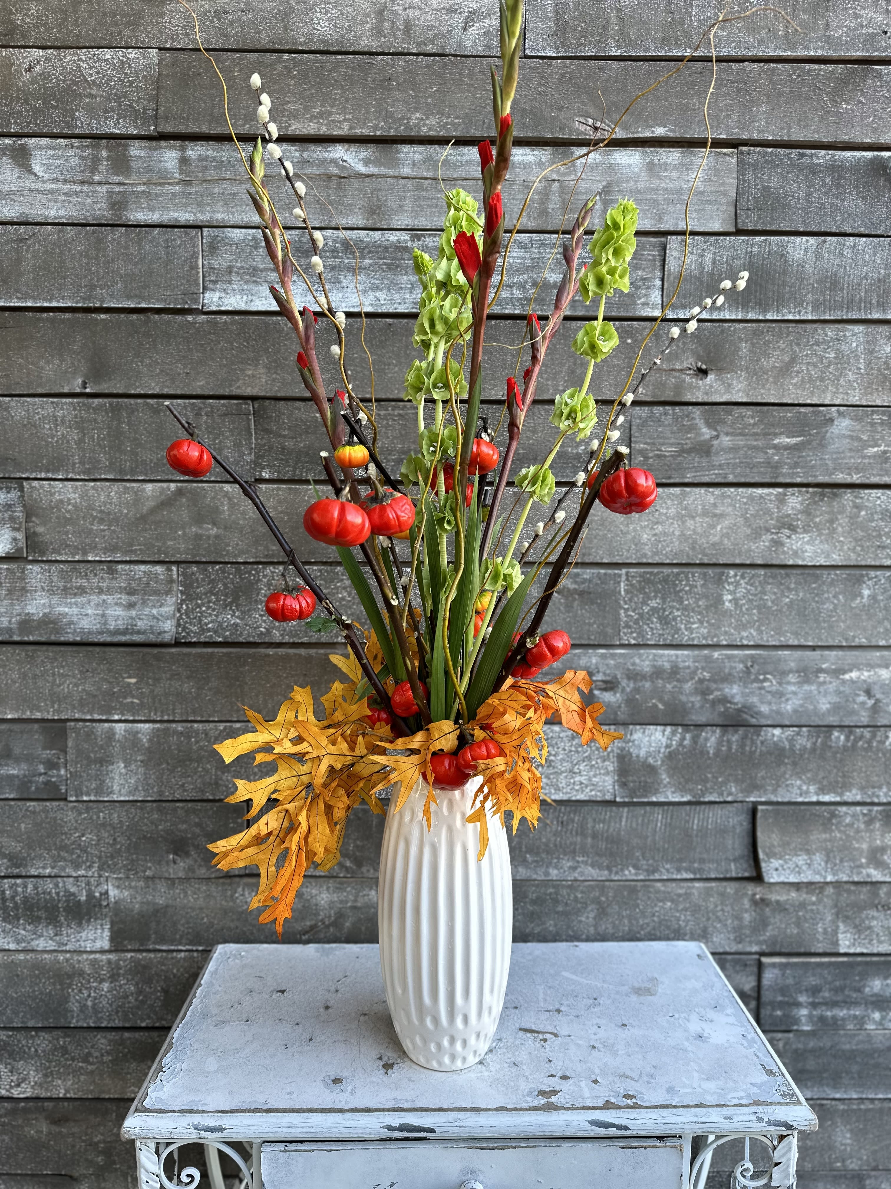 Tall autumn arrangement in a white vase with red and green accents