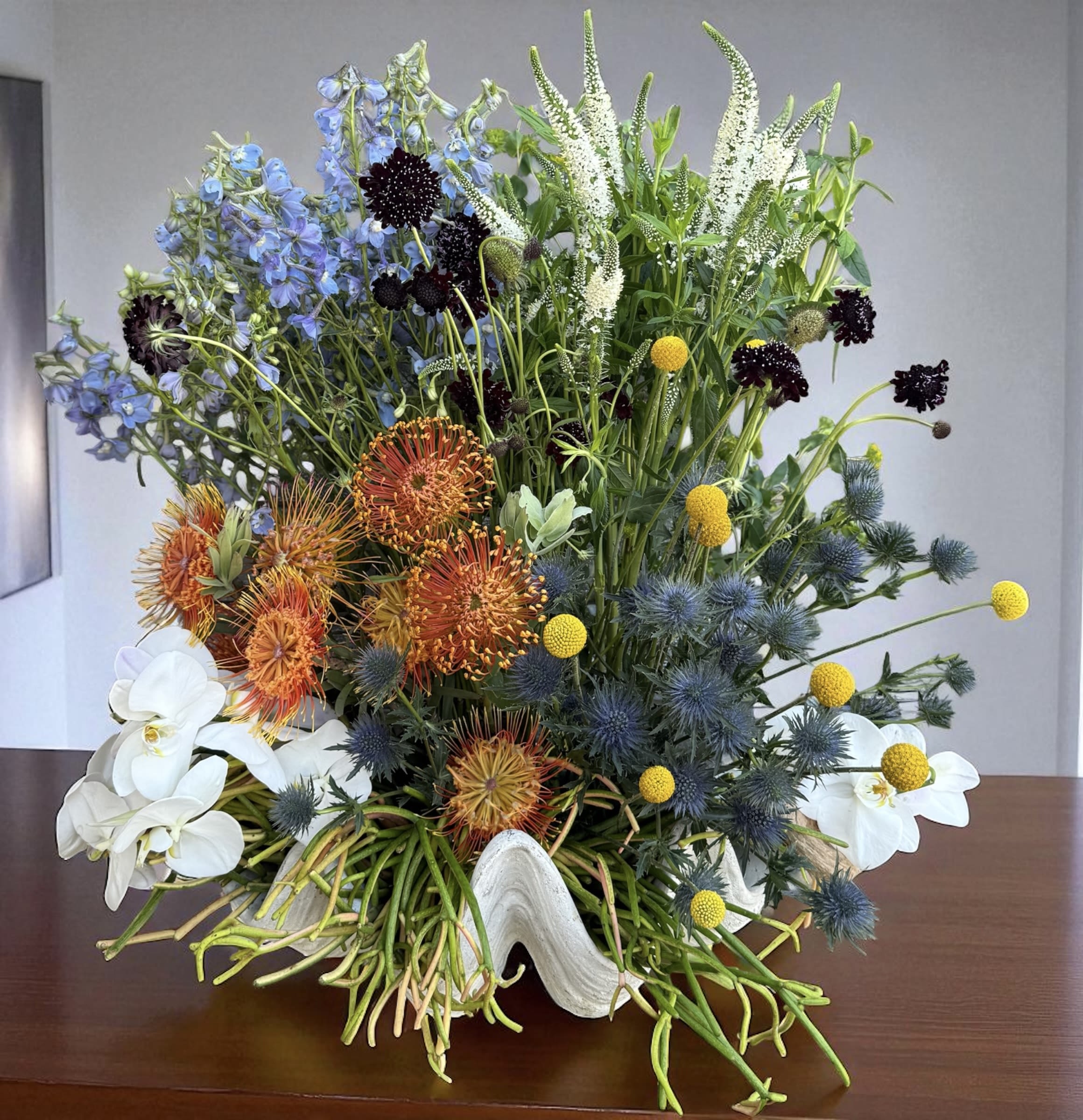 Mixed floral arrangement with blue, orange, white, and yellow blooms in a white vase